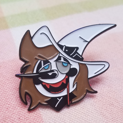 A cartoon-style pin of a witch with messy brown hair, a large white hat, and a mischievous smile, featuring a black, white, and red color scheme.