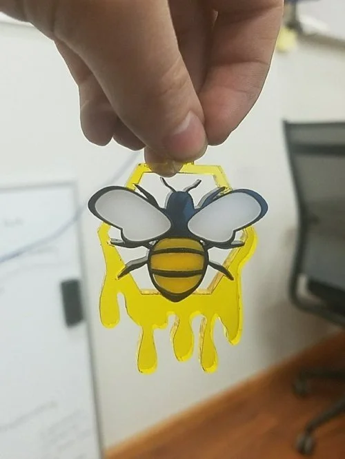 Hand holding a bee-shaped paper cutout with yellow paint drips on the bottom.
