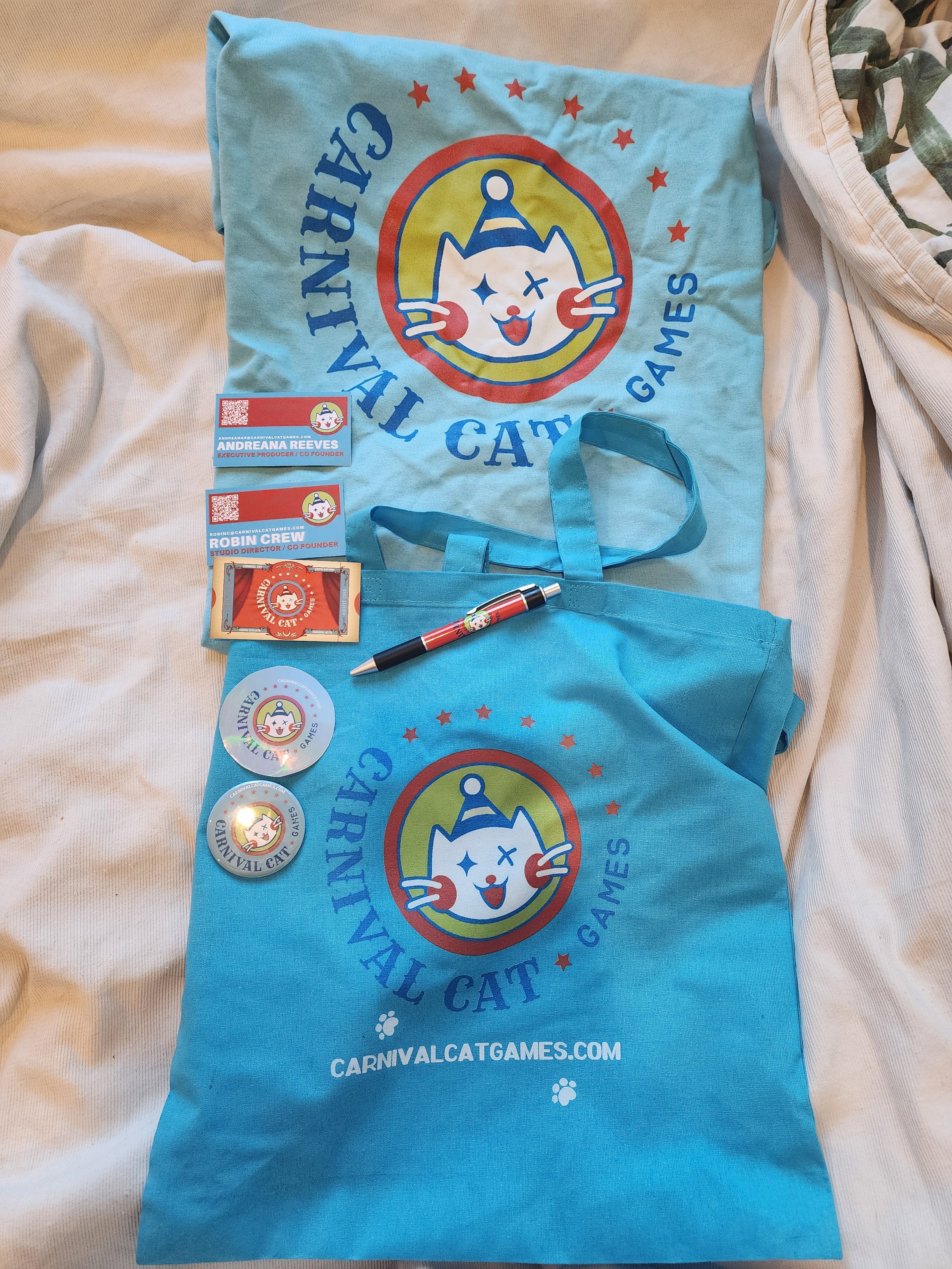 Blue promotional tote bag with the Carnival Cat Games logo, featuring a smiling cartoon cat with a party hat and a red circle. The bag displays the website carnivalcatgames.com and has red stars and small paw print icons.