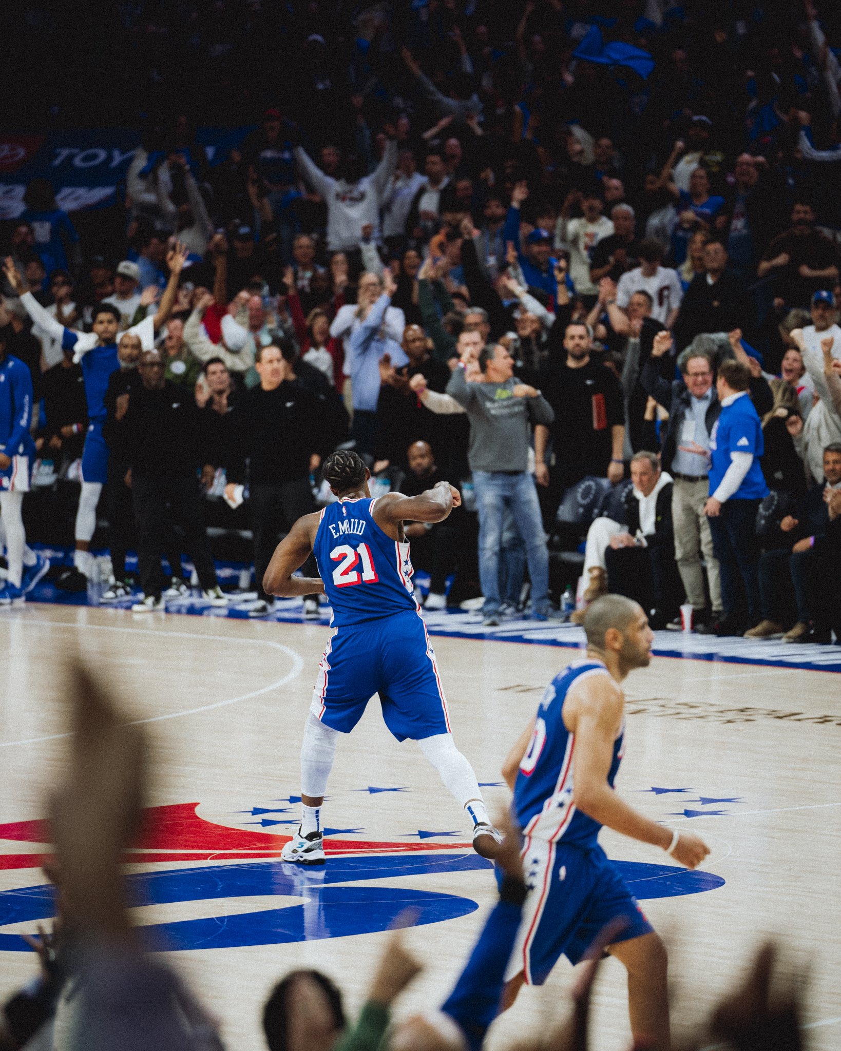 A basketball player in a blue uniform celebrating on the court after a game, with fans in the background cheering.