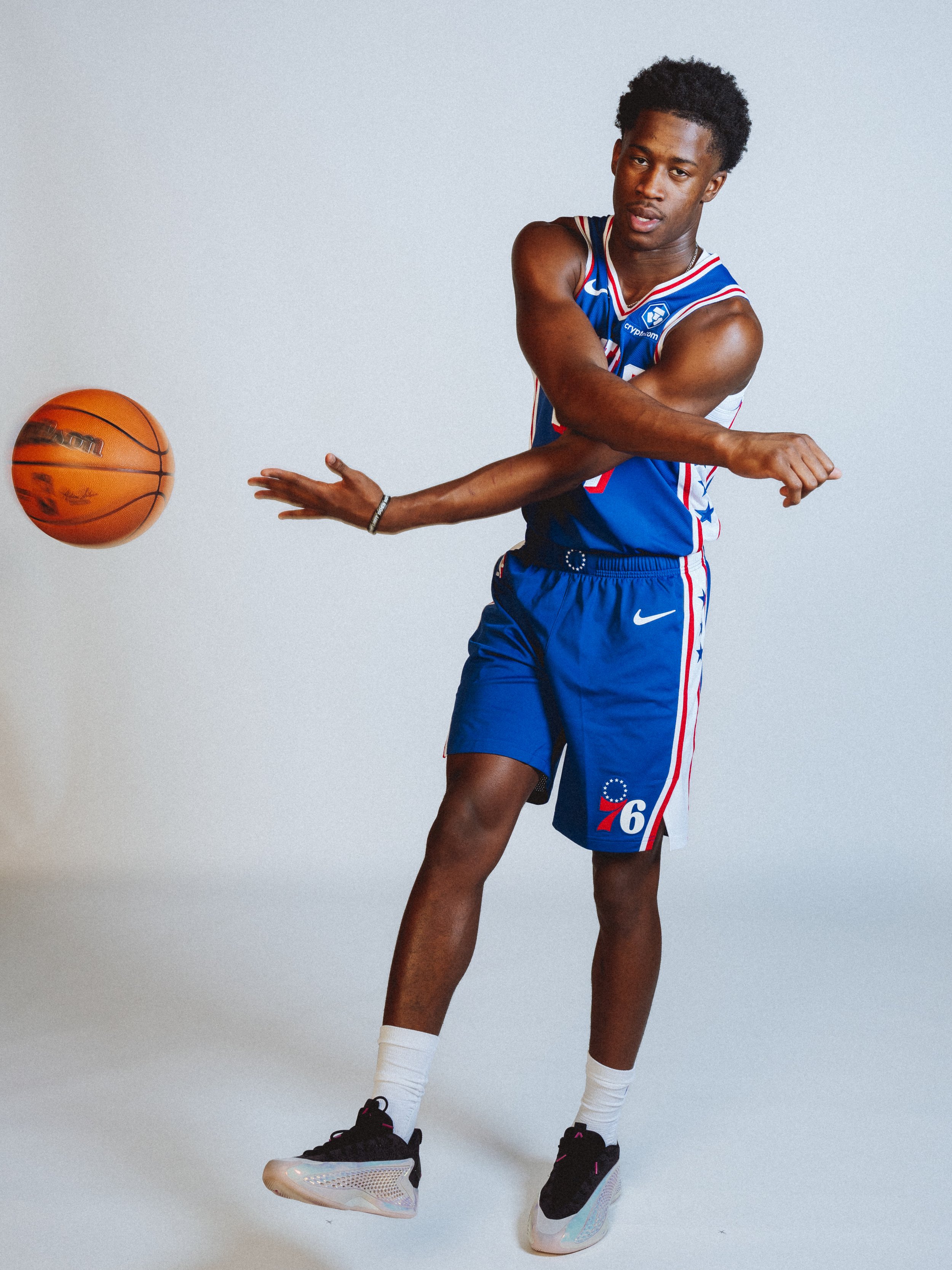 NBA Player,  VJ Edgecombe in a basketball uniform bouncing on a pair of iridescent sneakers against a plain white background.
