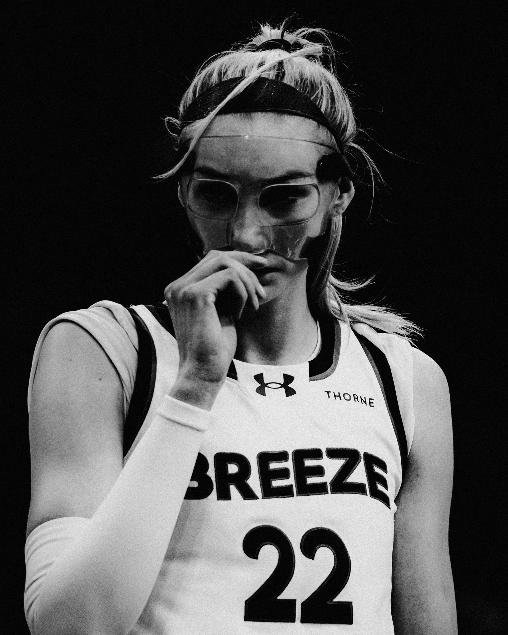 Close-up of a female athlete wearing glasses, a headband, and a sports jersey with the number 22, touching her face with her hand, against a dark background.