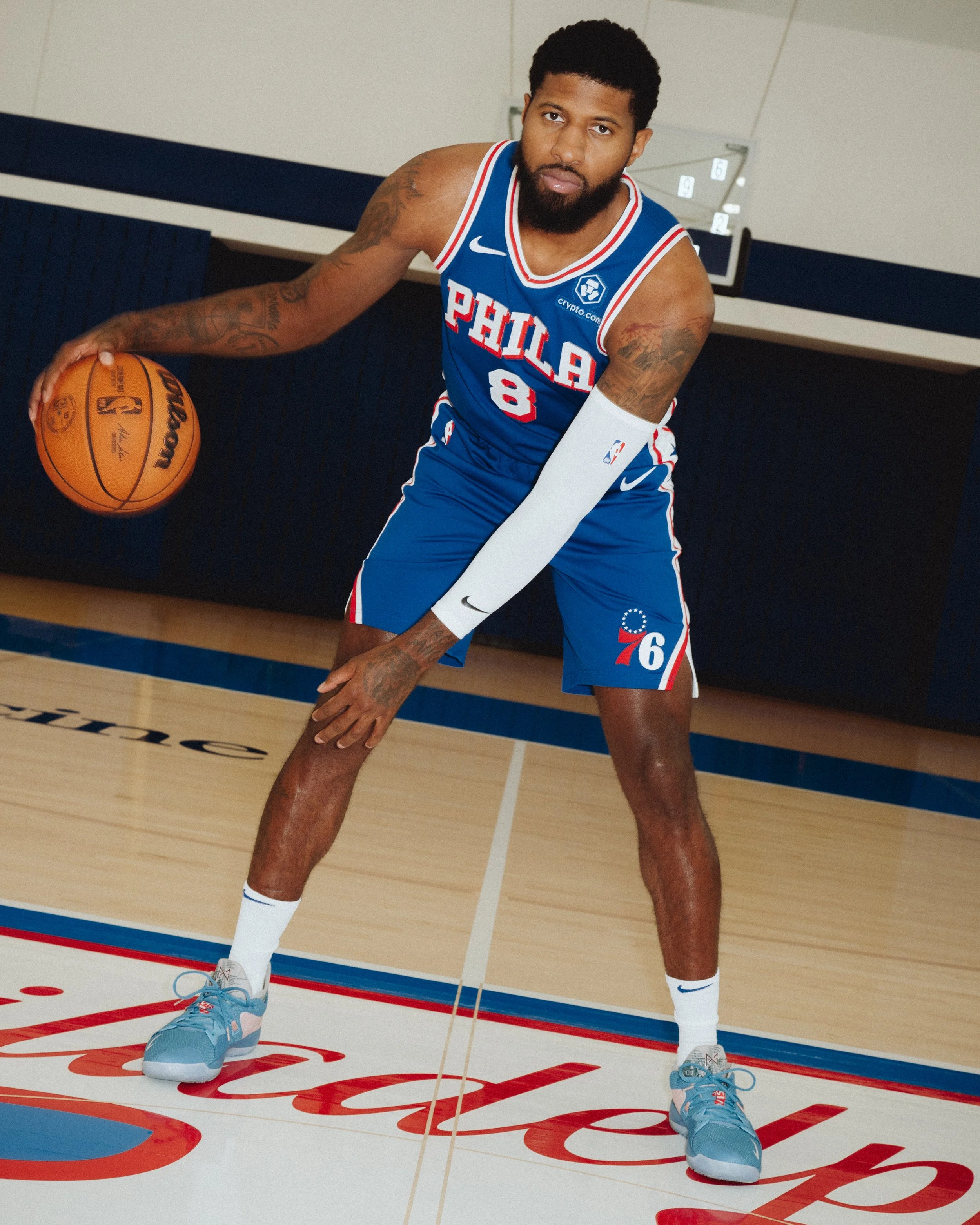 A professional basketball player wearing a Philadelphia 76ers uniform with the number 8, holding a basketball and standing on the hardwood court, with the team's logo and court markings visible.