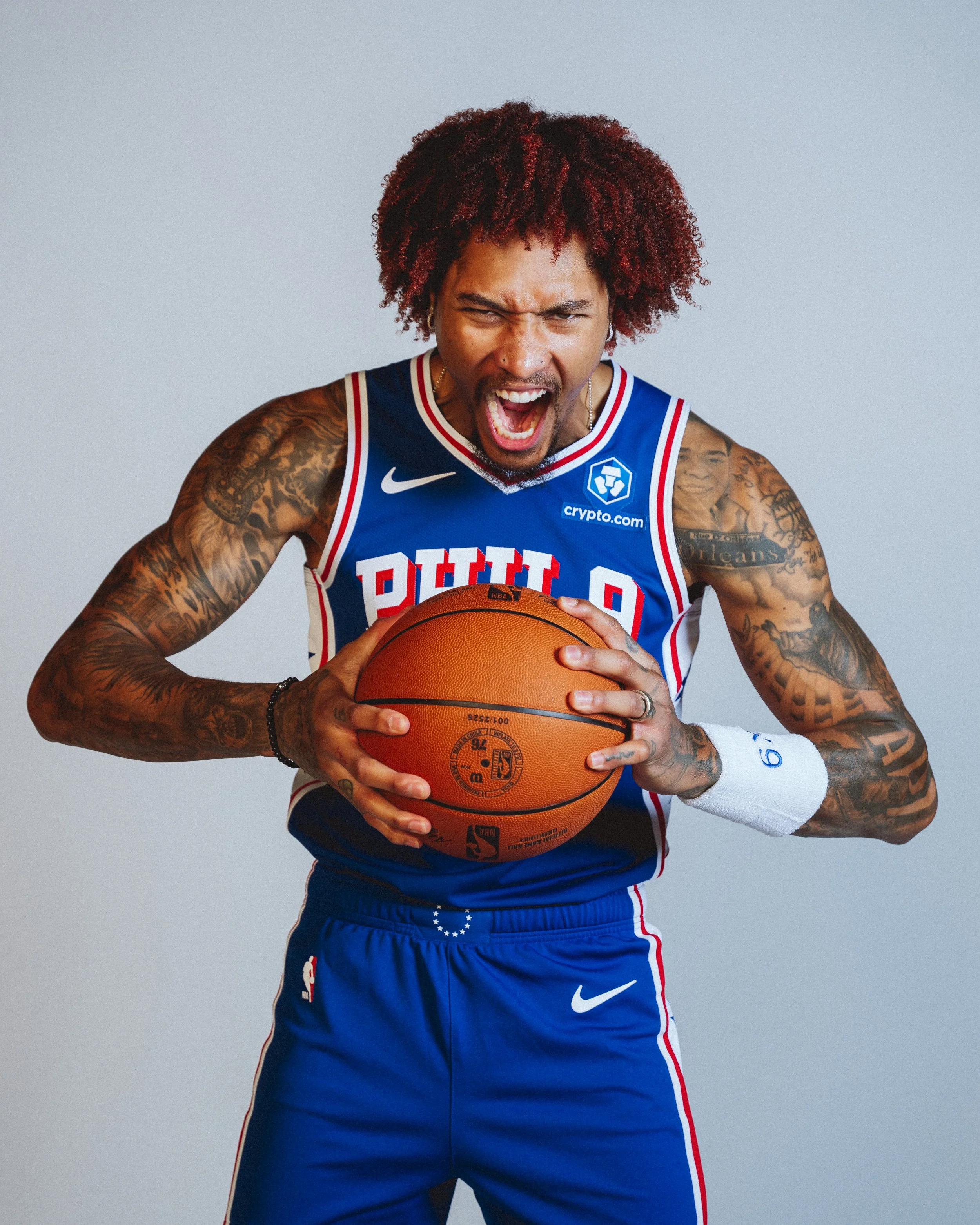 NBA Player,  Kelly Oubre in a Philadelphia 76ers basketball jersey holding an NBA basketball against a plain light gray background.
