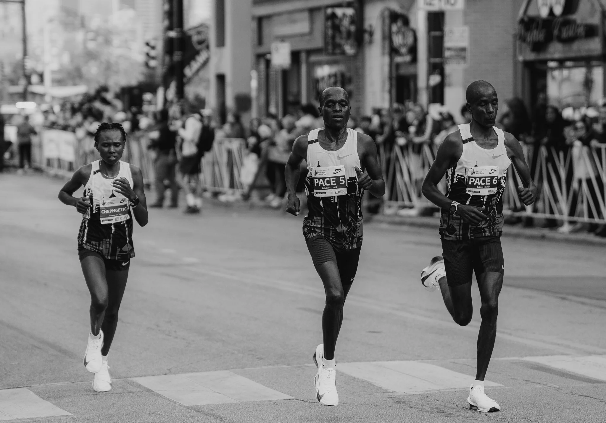 Black and white photo of three marathon runners running on a city street with spectators behind barricades.