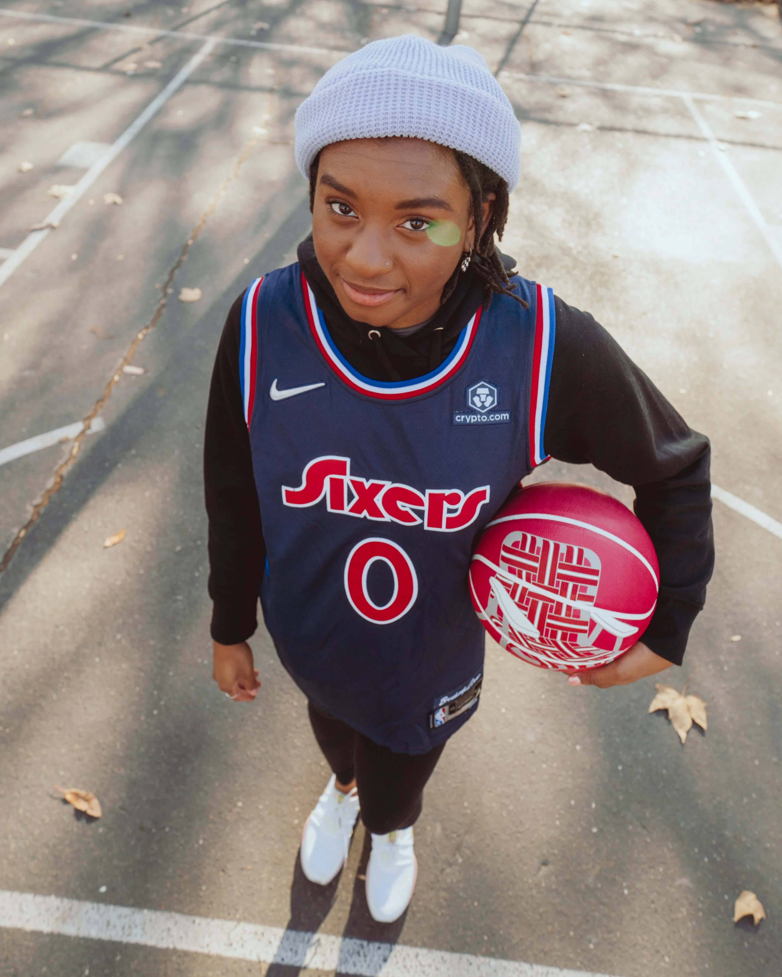 A young person holding a pink basketball outdoors on a paved court, taken from a top angle.