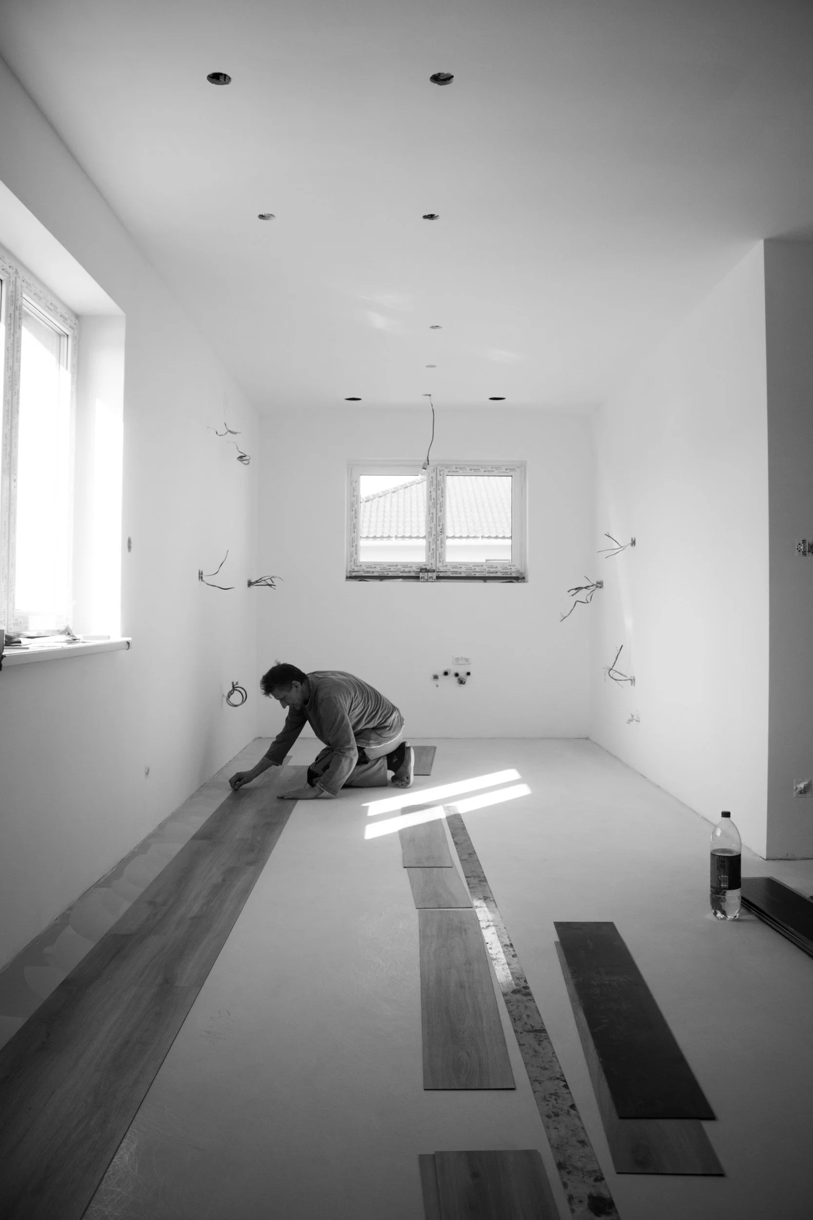 A person installing wooden flooring in a room with white walls and a window, using tools and laying out planks on the floor.