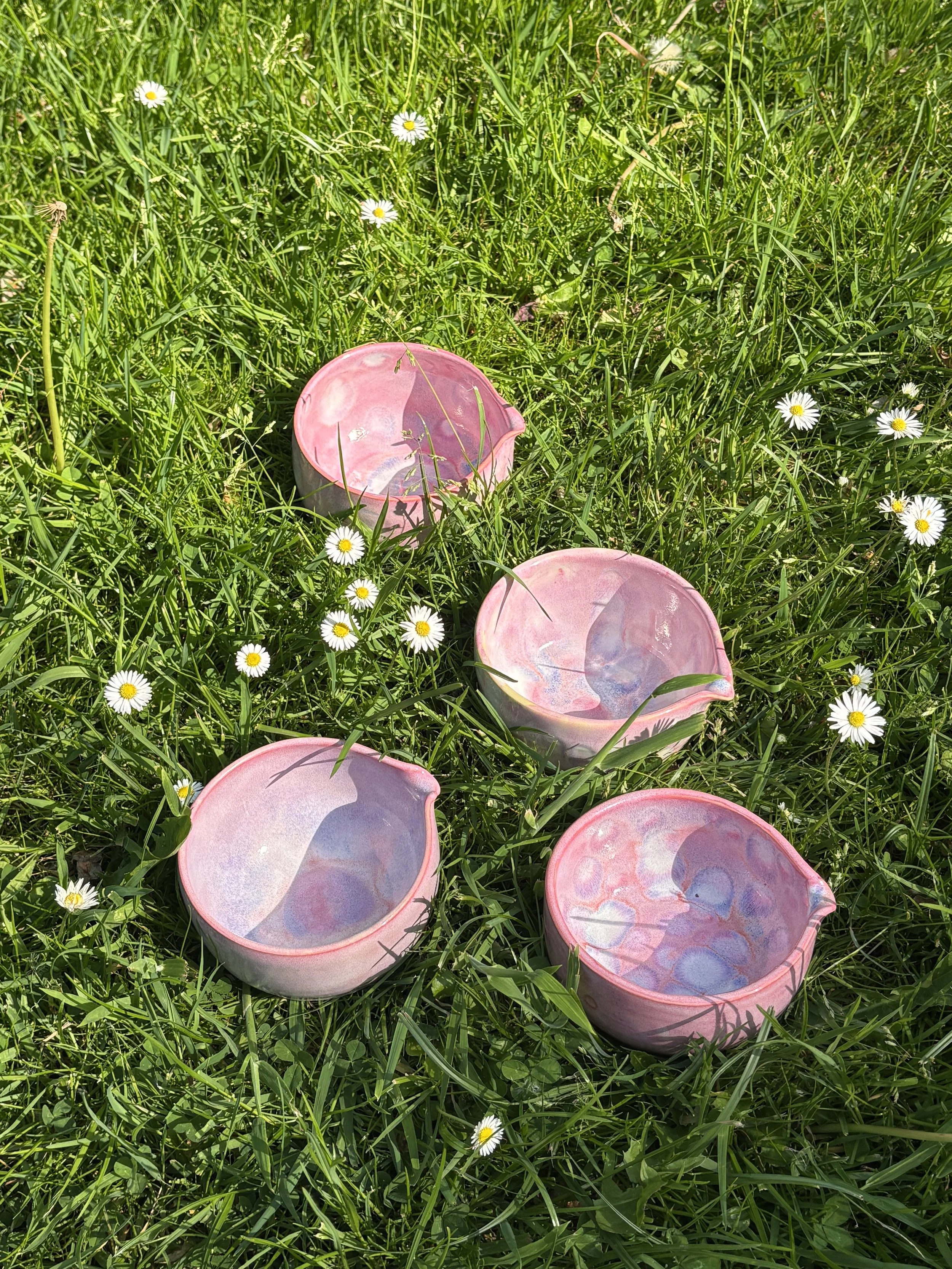 Pink ceramic matcha bowls placed on green grass with small white daisies scattered around.
