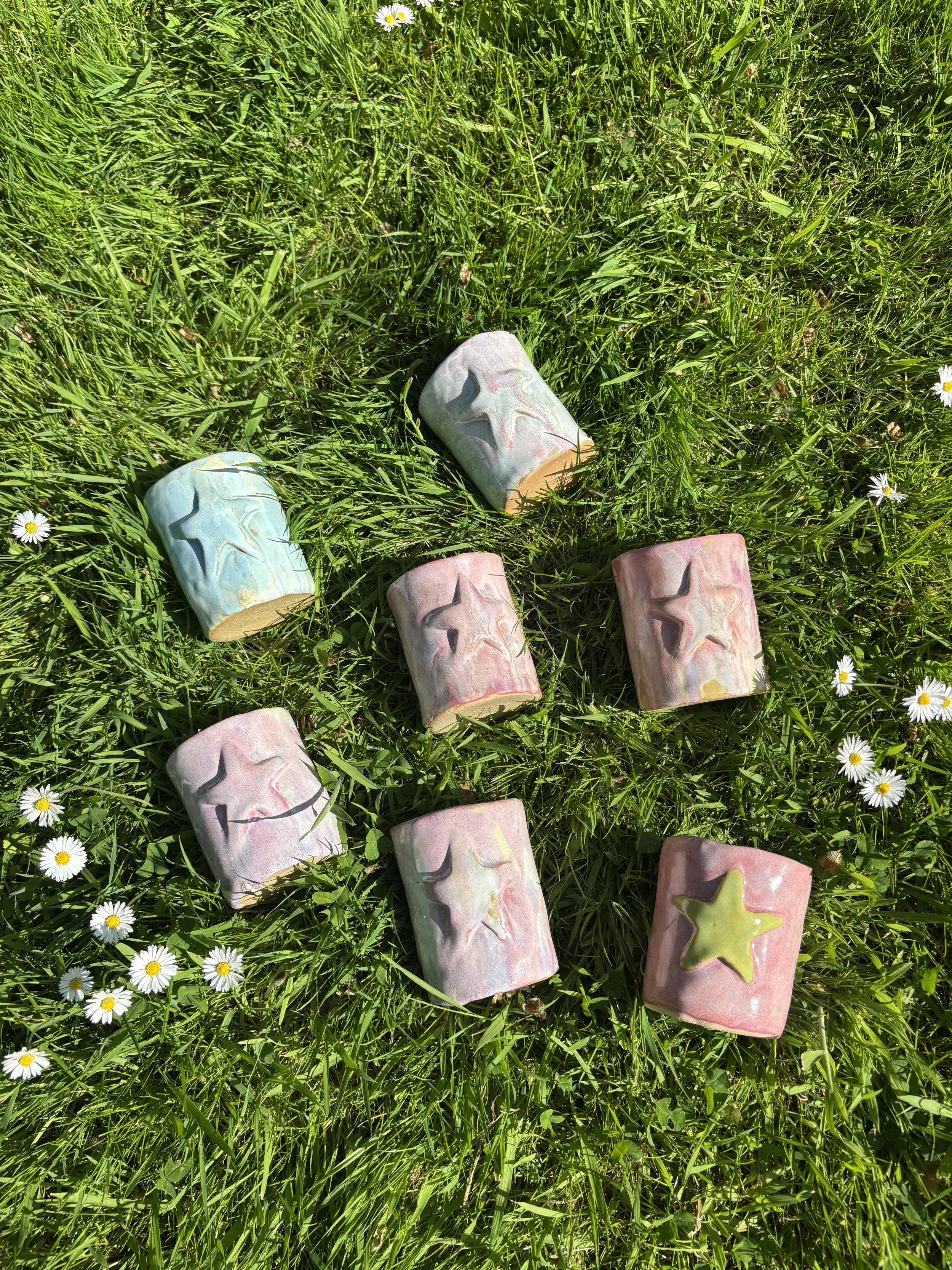 Colorful ceramic cups with star design on green grass with small white daisies.