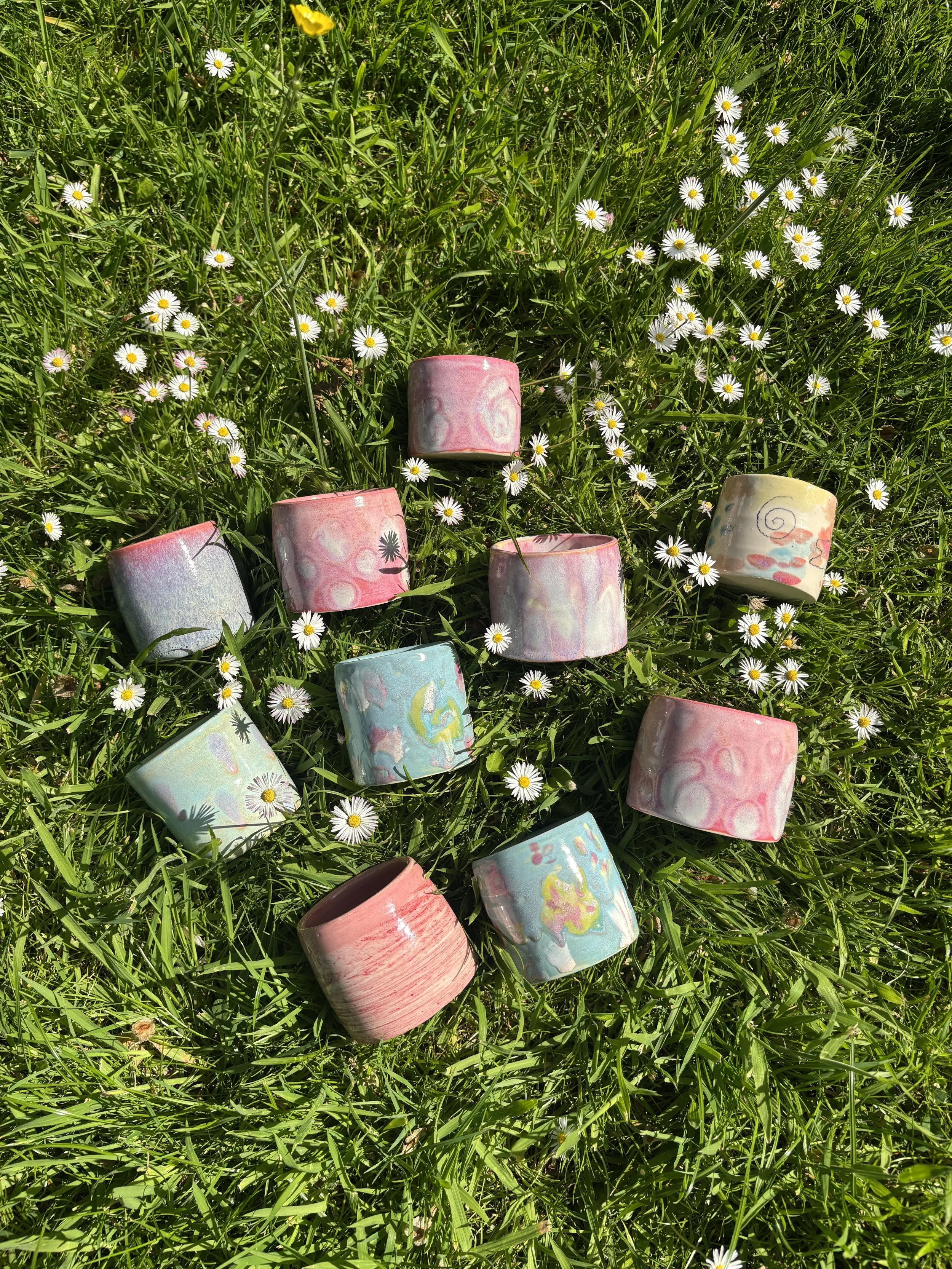 Colorful ceramic mugs scattered on green grass with small white daisies.