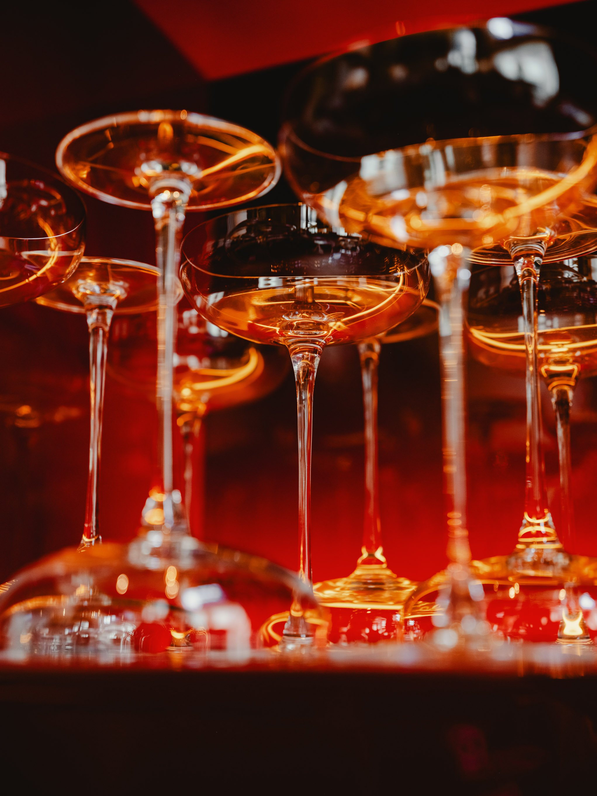 Multiple upside-down champagne glasses with a warm amber glow, reflecting lights, and a dark background.