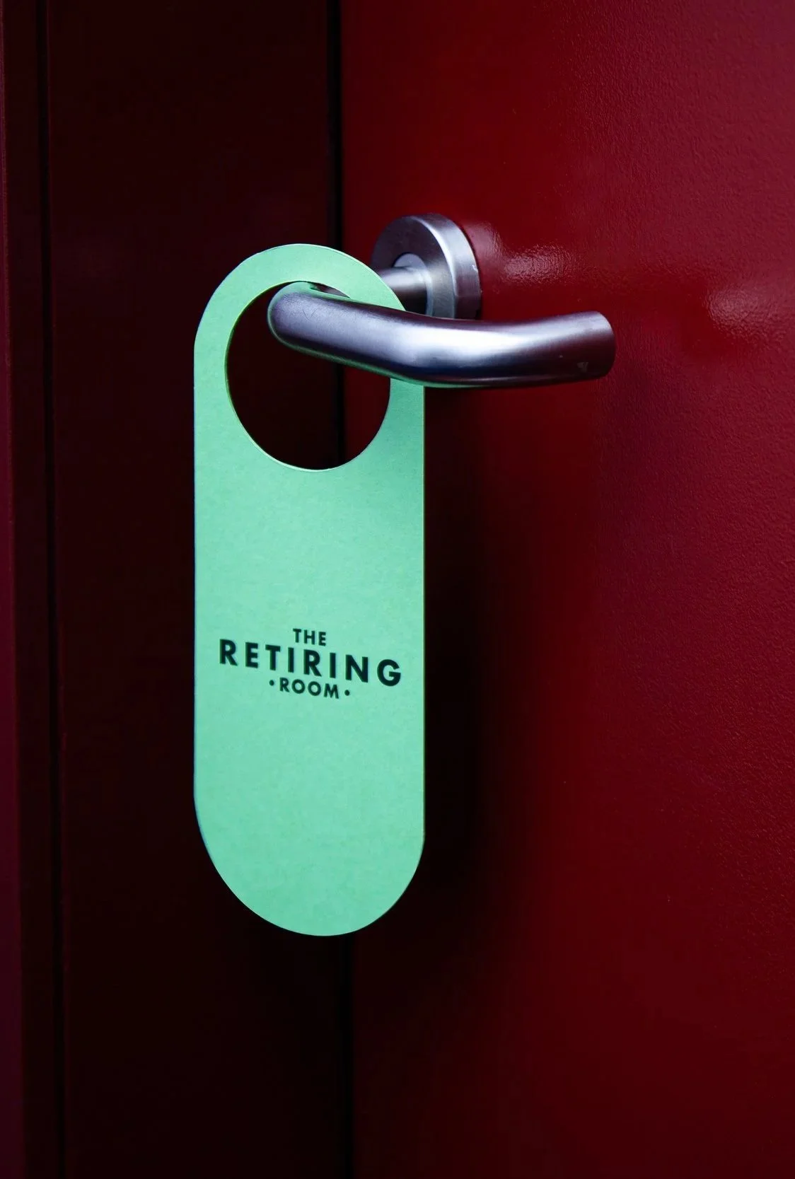 Green door hanger with a circular cutout and black text that reads 'The RETIRING ROOM',