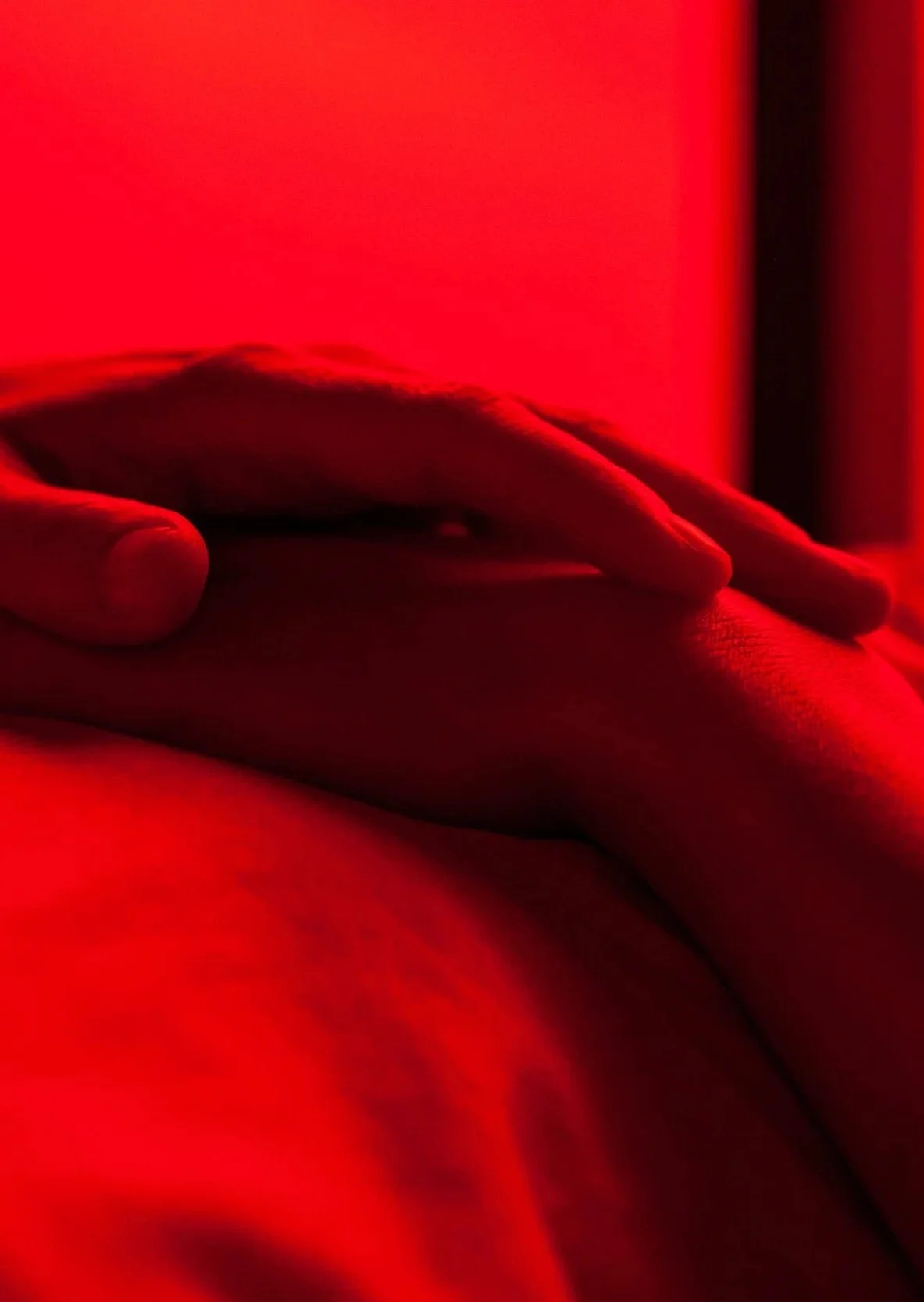 Close-up of a person's hand resting on their torso with red lighting in the background.