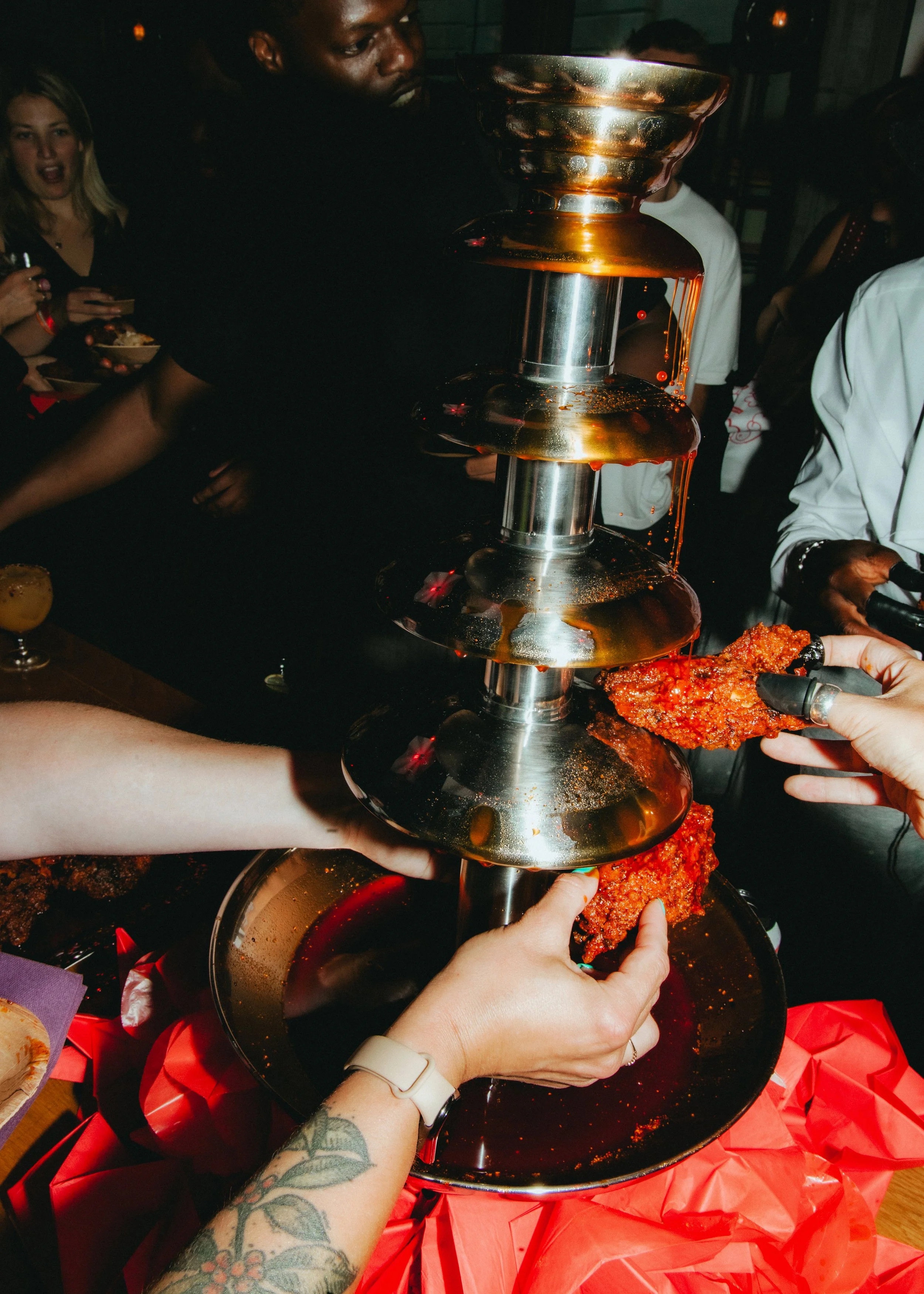 People at a party with a chocolate fountain, dipping a piece of cake into the chocolate.