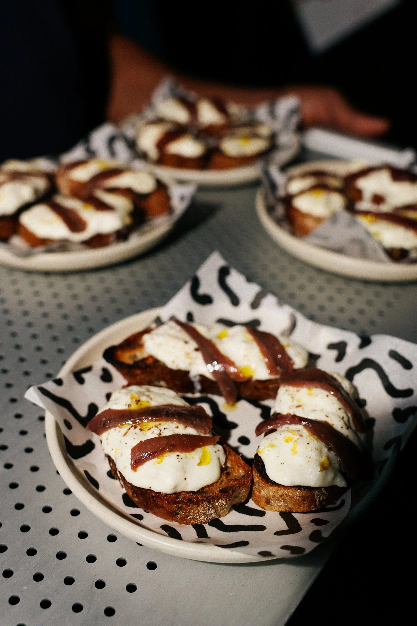 Close-up of cups filled with toasted bread topped with mozzarella cheese, strips of cured meat, lemon zest, and a drizzle of balsamic glaze.