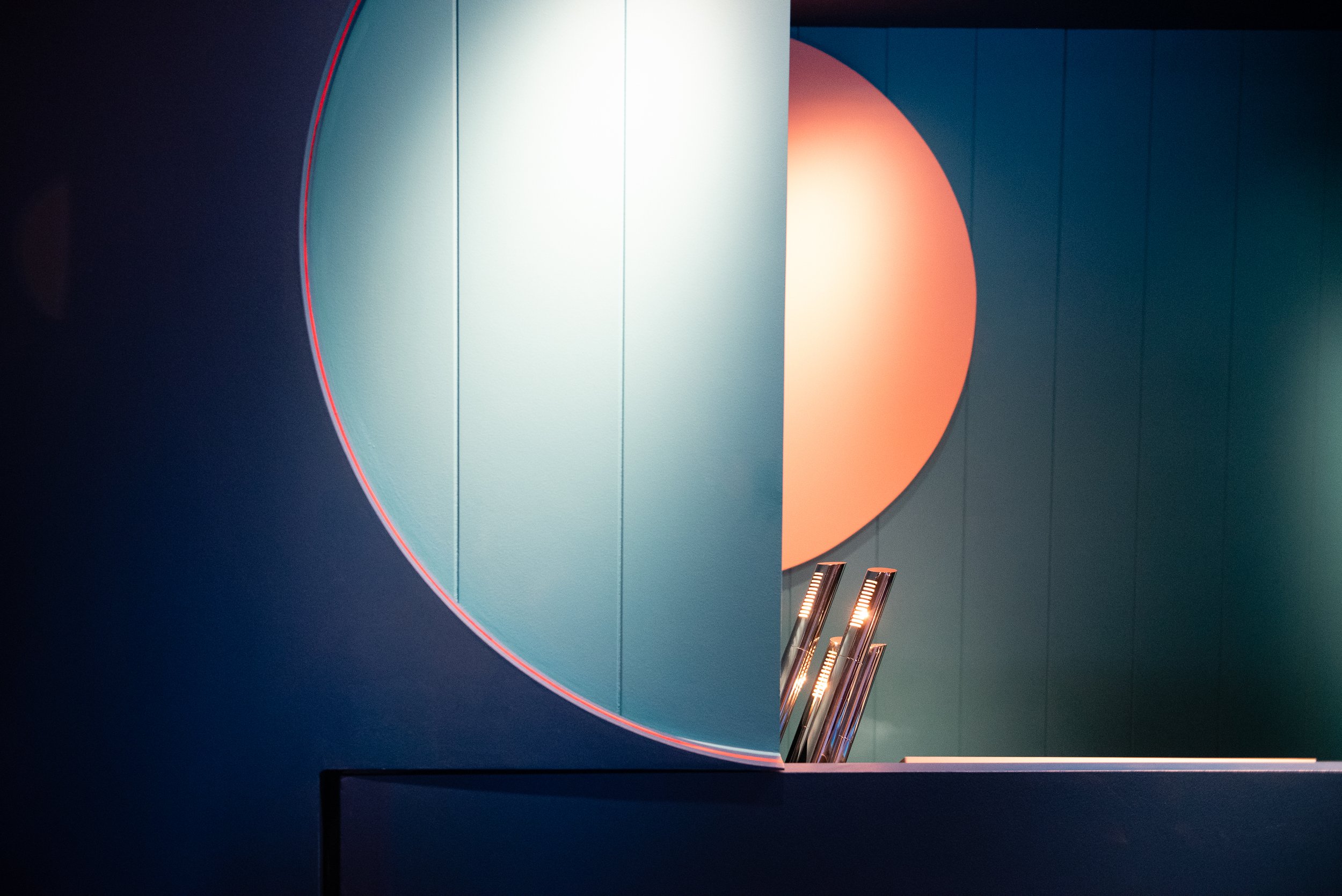 Interior view of a modern building with a teal wall, illuminated orange semicircle, and recessed lighting fixtures.