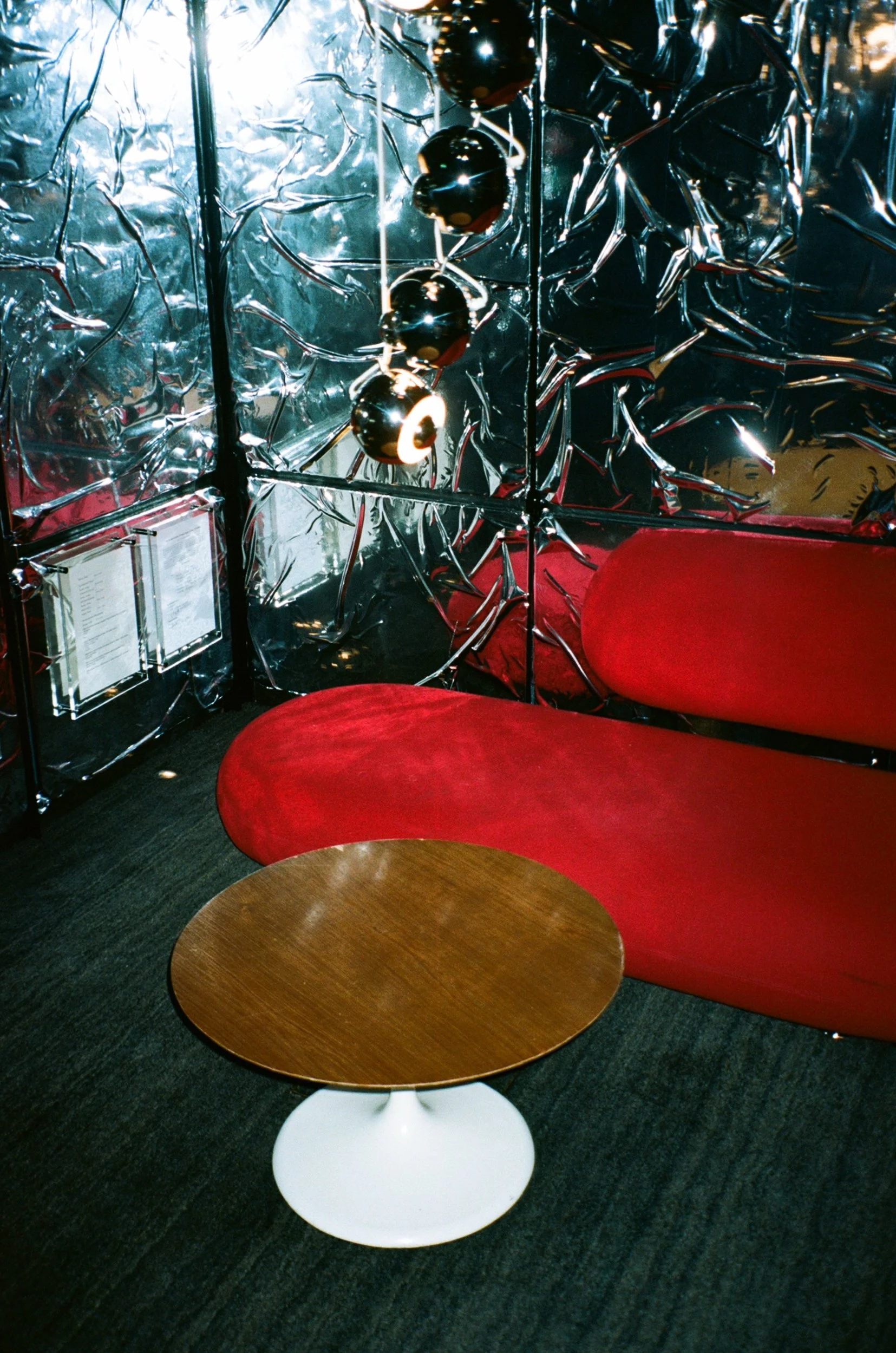 Interior of a room with crinkled metallic reflective walls, red seating, and a wooden table with a white pedestal base.