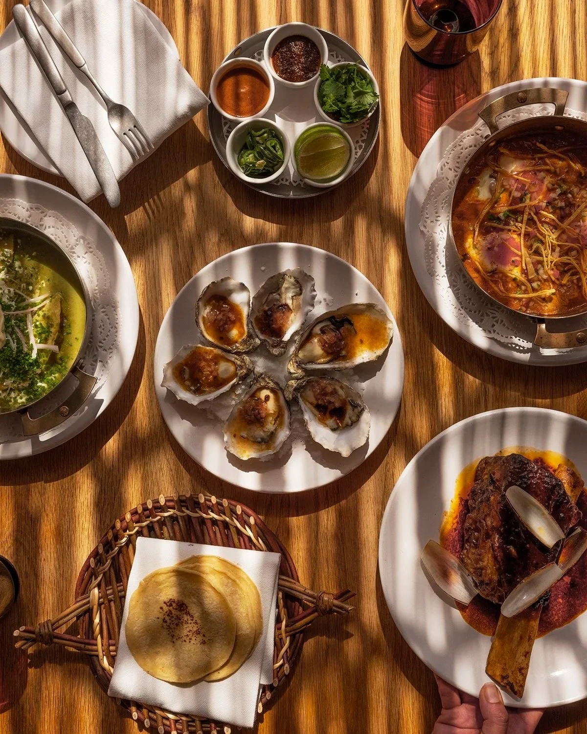 Table with various dishes including oysters with sauce, soup, naan bread, and a glass of red wine.
