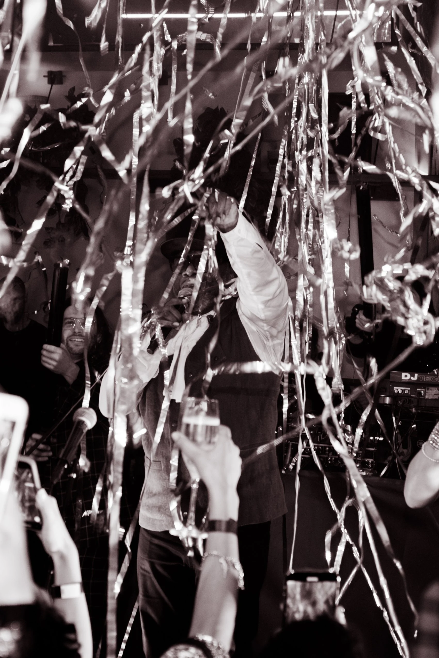 People celebrating with metallic streamers at a party or event, with some individuals holding drinks and using a microphone.