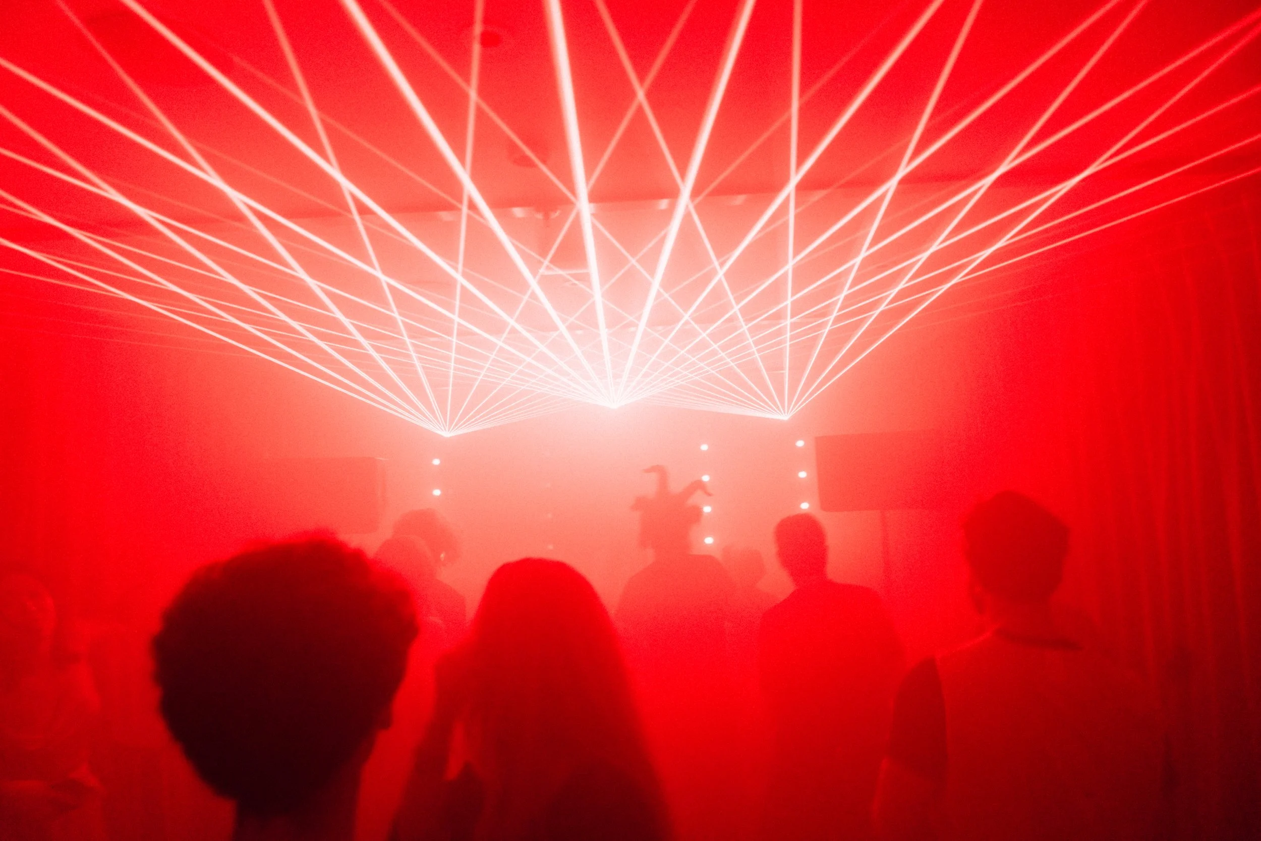 People attending a concert or event with red laser lights in the background.