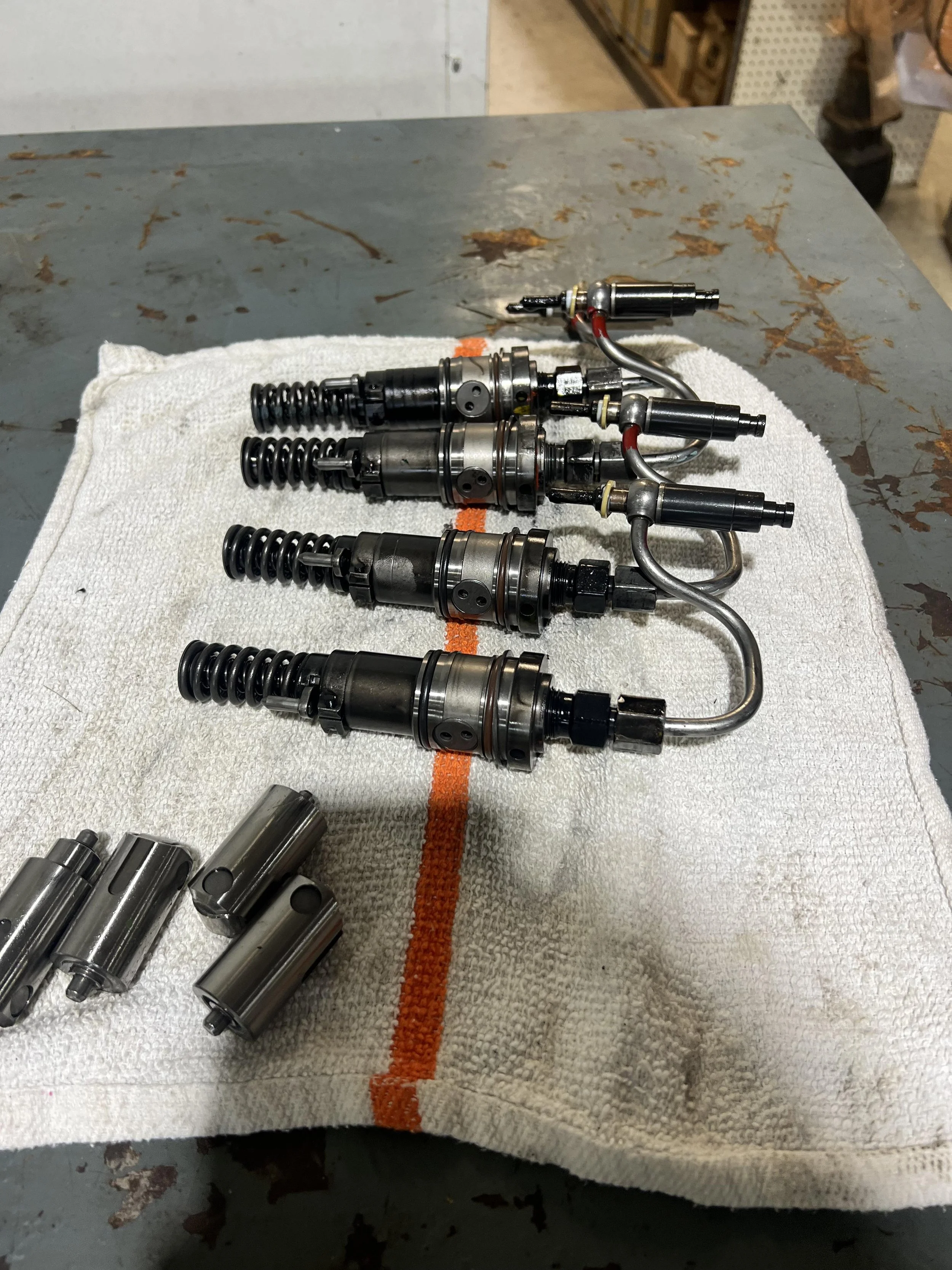 A set of fuel injectors arranged on a white towel with an orange stripe, placed on a workbench with a gray, worn surface.