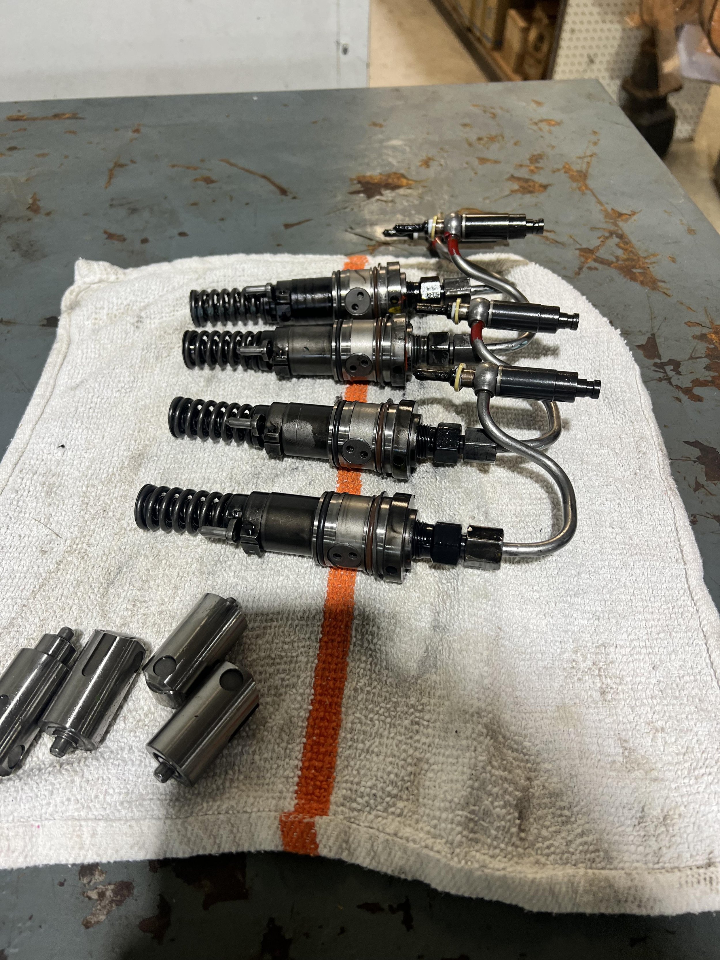 Four fuel injectors lay on a white towel on a workbench, with additional parts nearby.