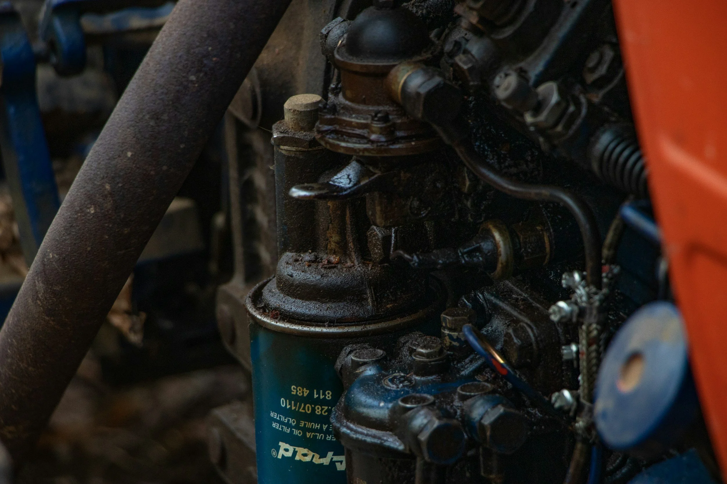 Close-up of a rusty mechanical engine component, with parts covered in grease and dirt, surrounded by various mechanical elements and a blue filter.