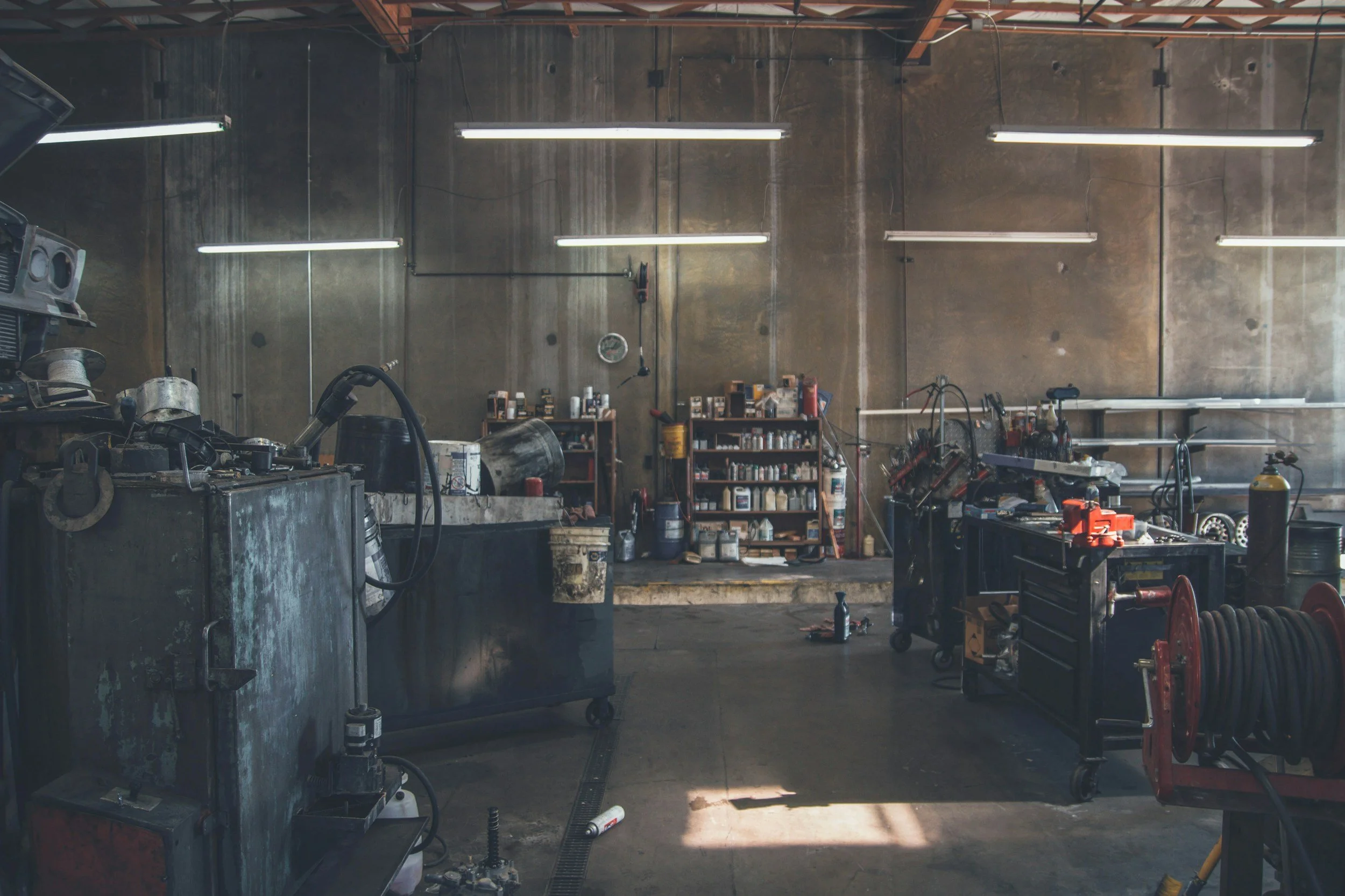 Inside a cluttered mechanic or workshop with tools, shelves filled with supplies, and workbenches.