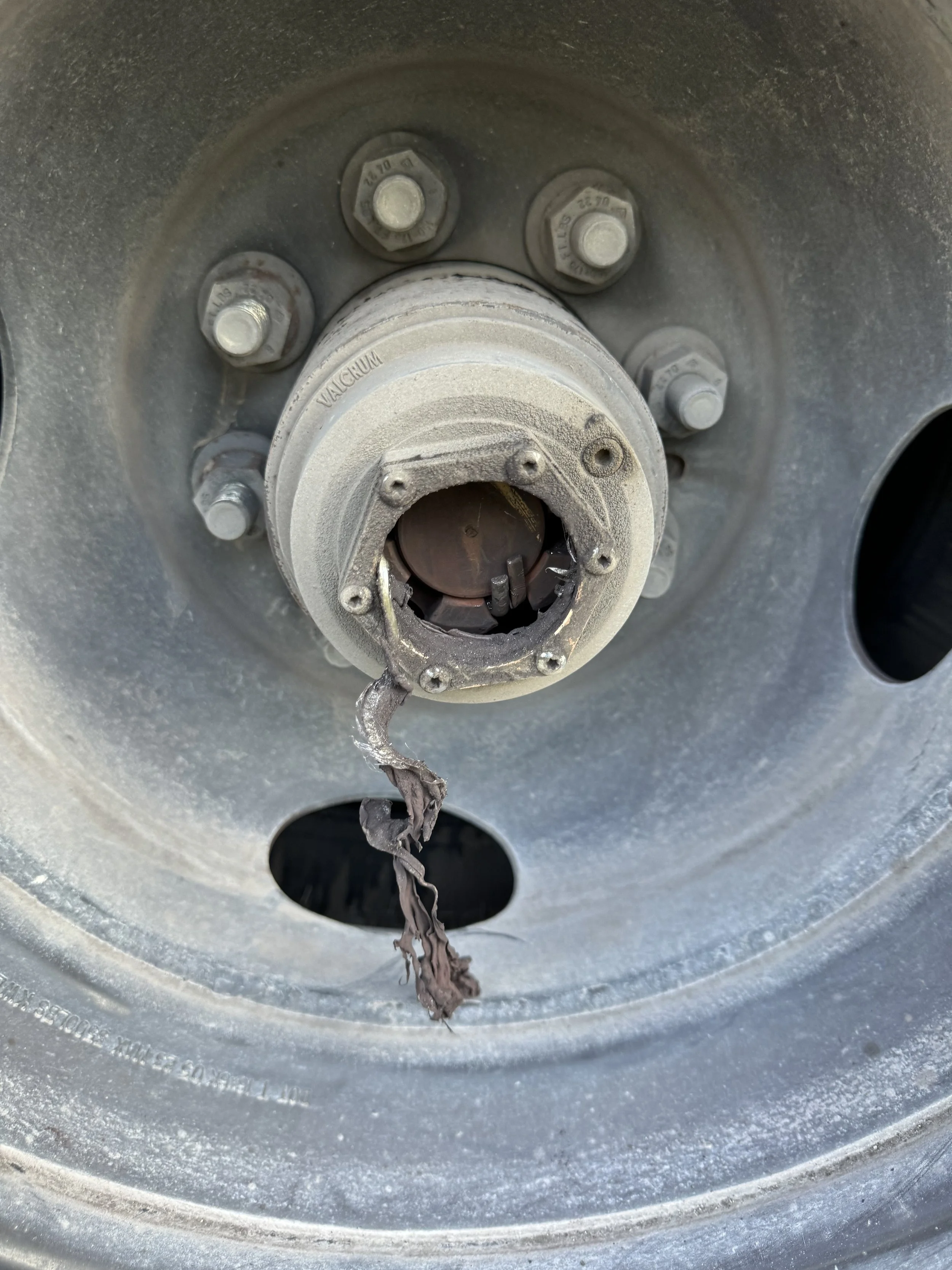 Close-up of a vehicle wheel hub with the lug nuts and the brake rotor visible behind, and some thread debris hanging from the hub.