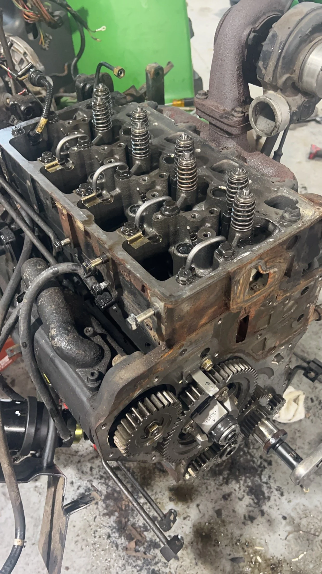 Automobile engine with exposed gears and valves, partially disassembled, on a workbench in a workshop.