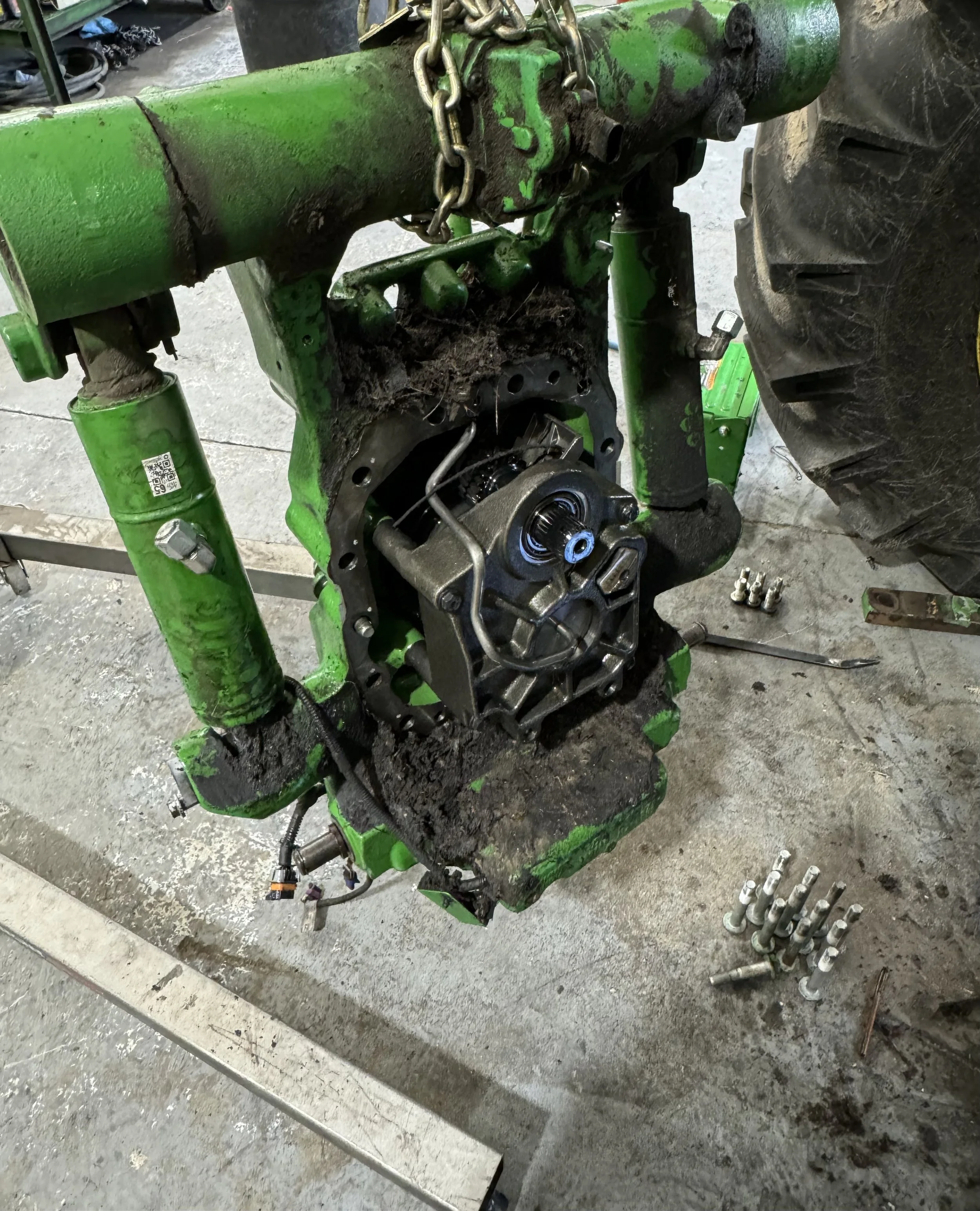 Close-up of a green tractor engine with some parts removed, exposing inner mechanical components, with a set of bolts on a nearby flat surface.