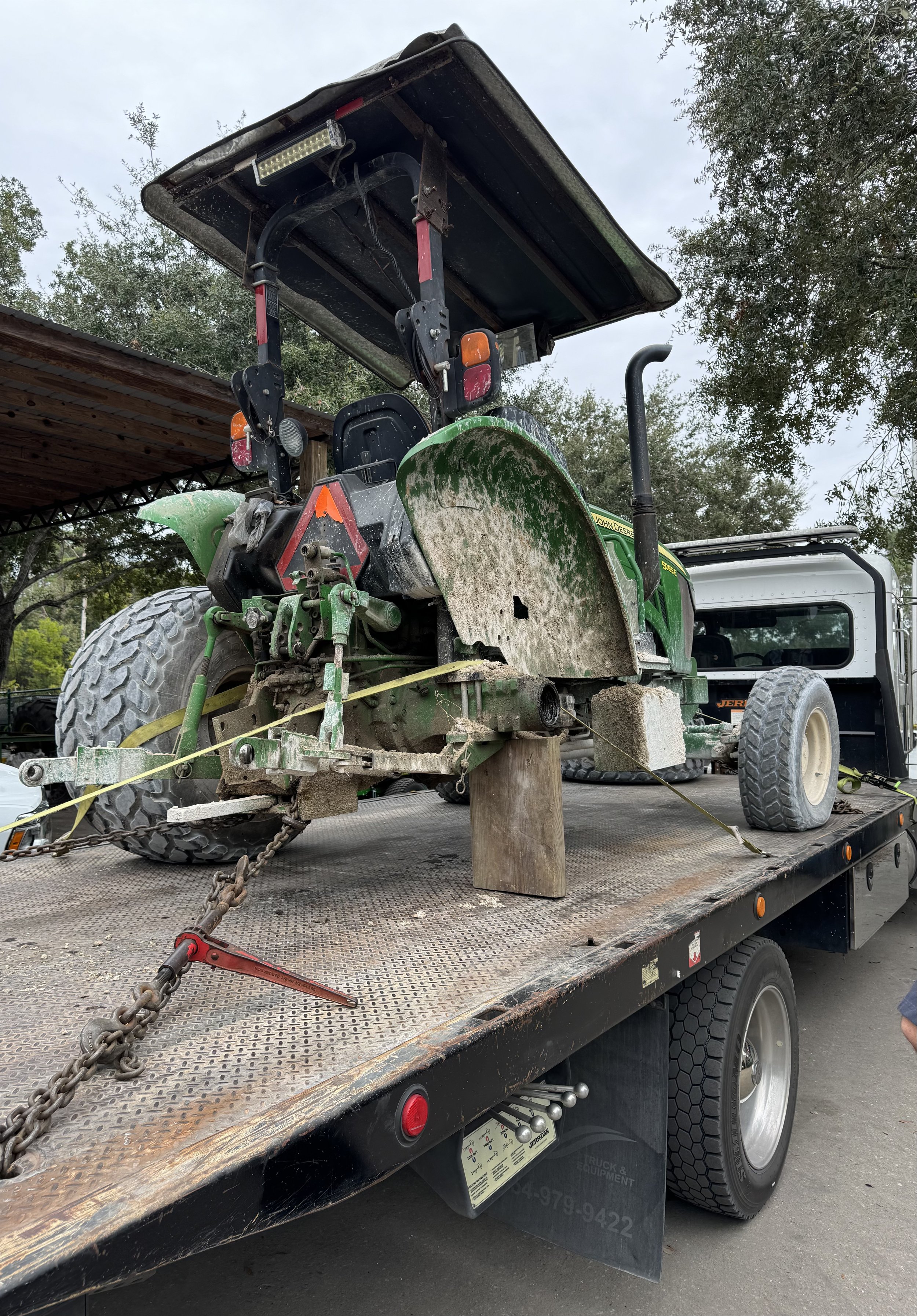 A John Deere green and yellow lawnmower with a large cutting blade mounted on a flatbed truck.