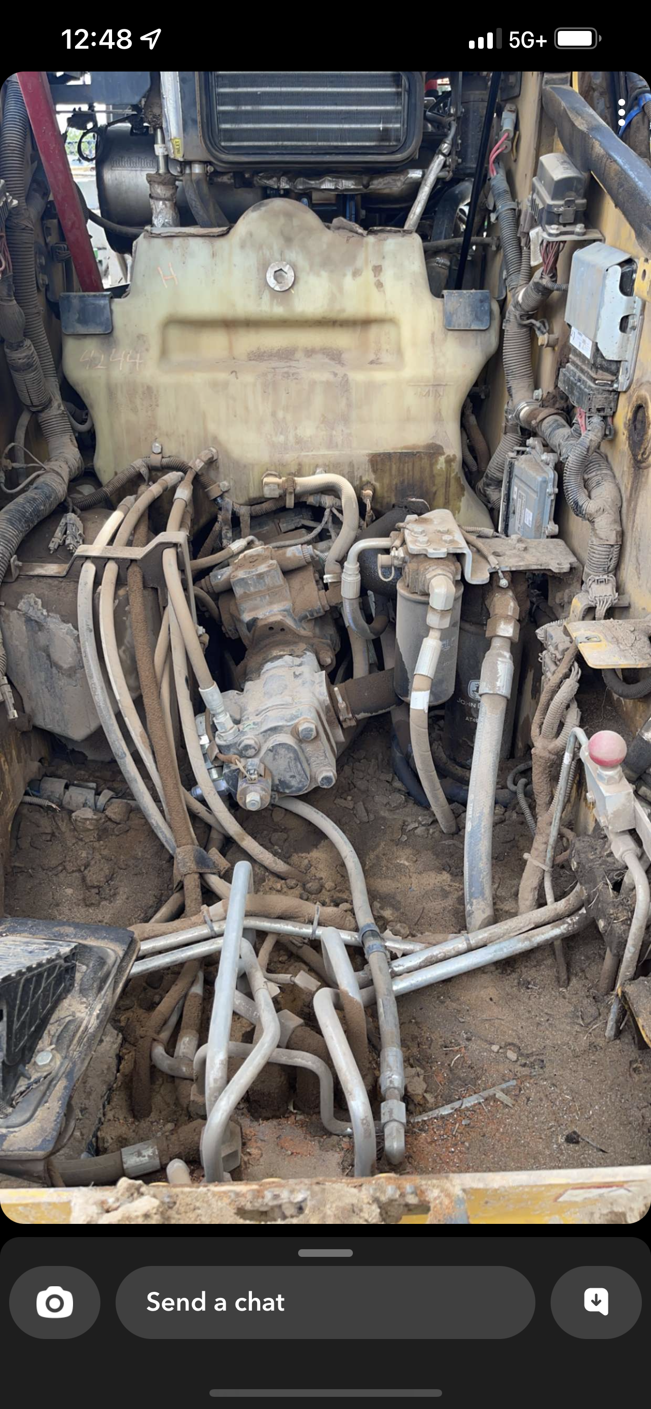 Close-up view of an engine compartment with various hoses, wires, and components covered in dirt and dust.