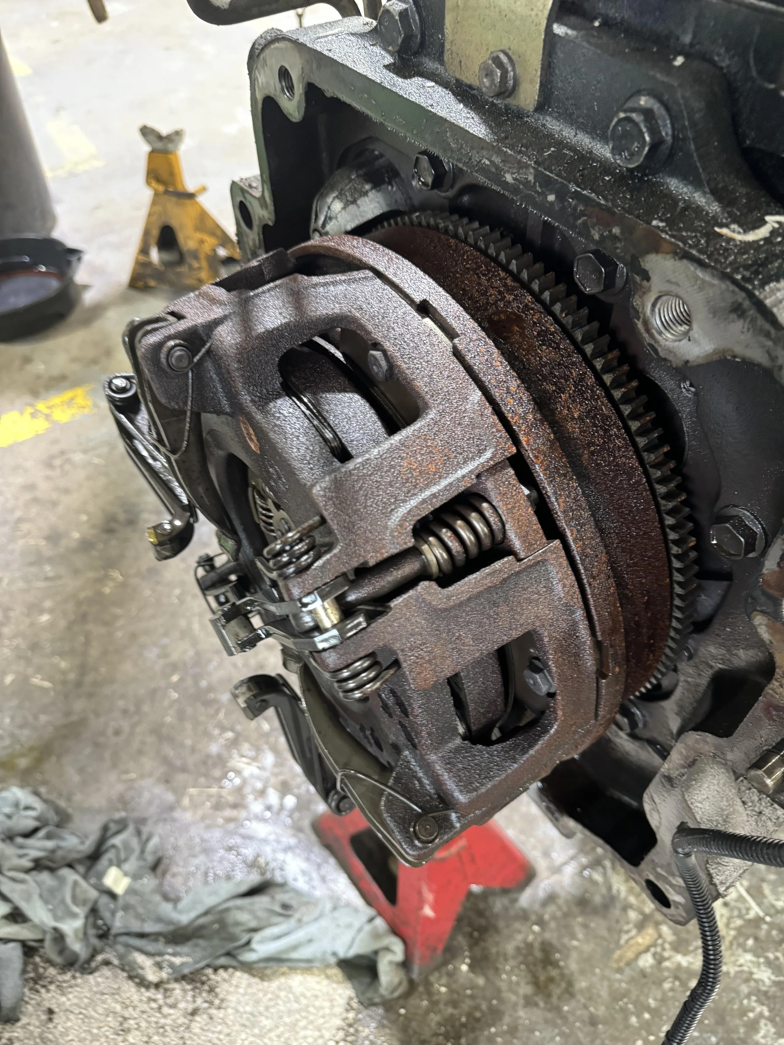 Close-up of a disassembled automotive transmission or engine component showing gears, springs, and metal parts on a workshop floor.