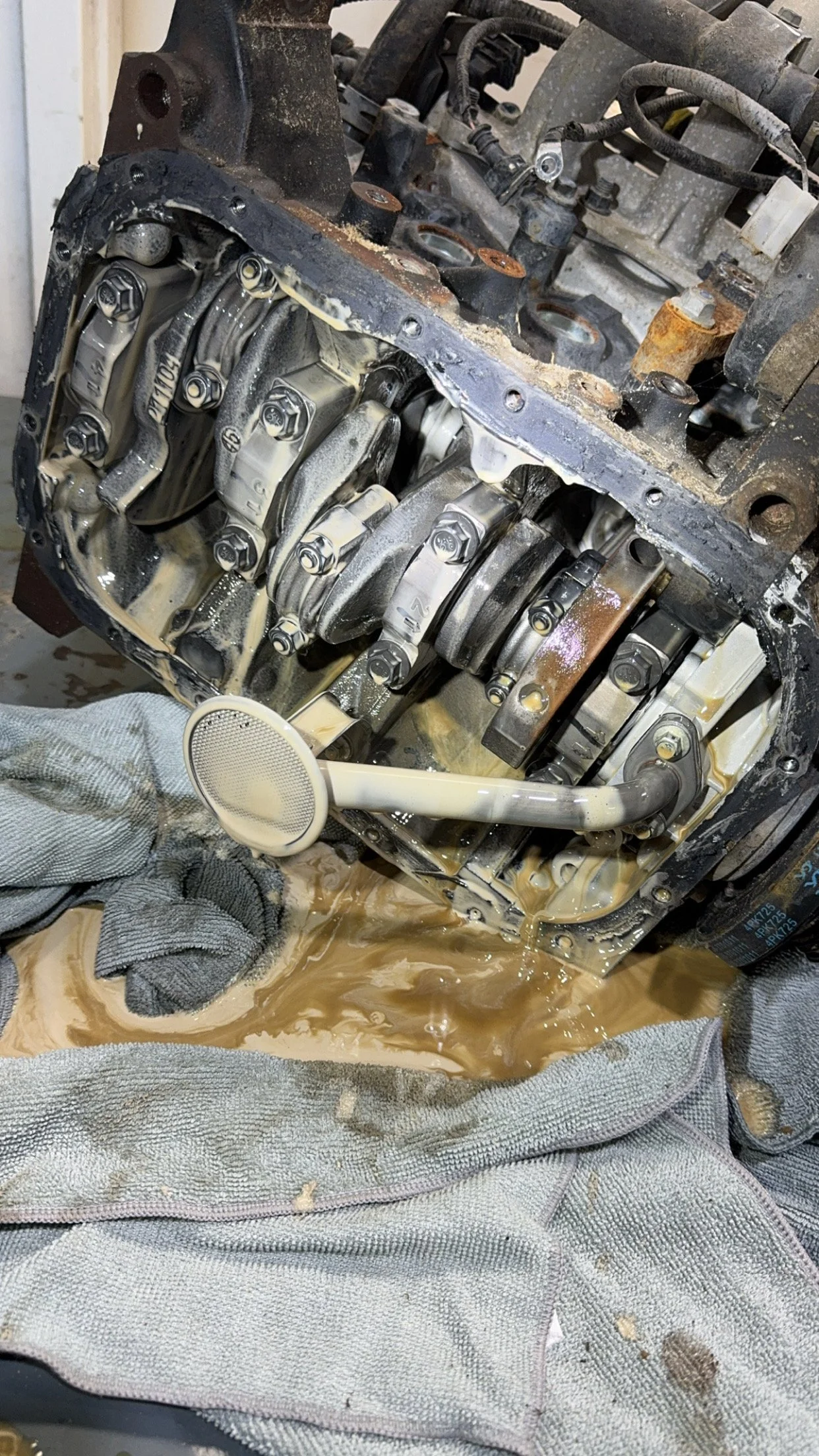 Open engine of a vehicle with internal components exposed, wet with oil and fluids, resting on a cloth.
