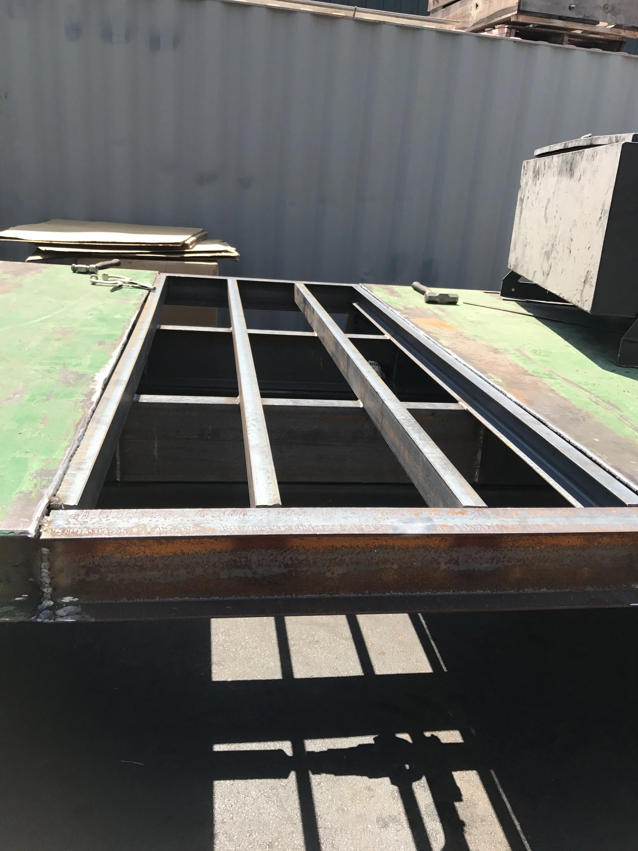 A partially assembled metal frame or structure on a flat surface, with tools like a wrench and a hammer nearby, casting shadows on the ground.