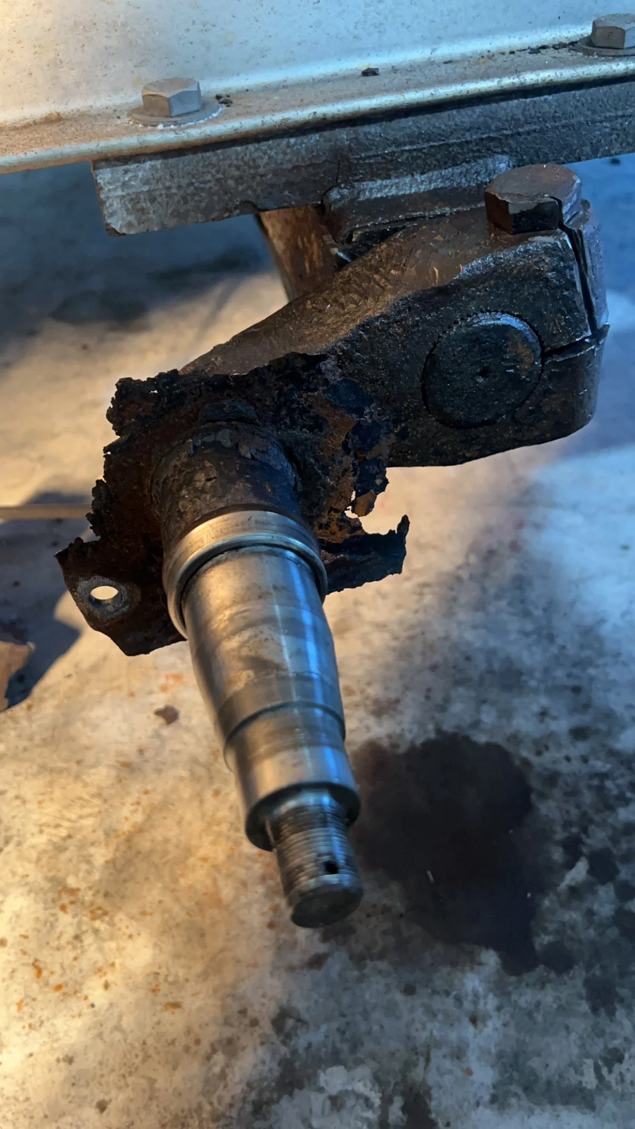 Close-up of a rusty, broken mechanical component attached to a metal rod, with bolts and a supporting structure above.