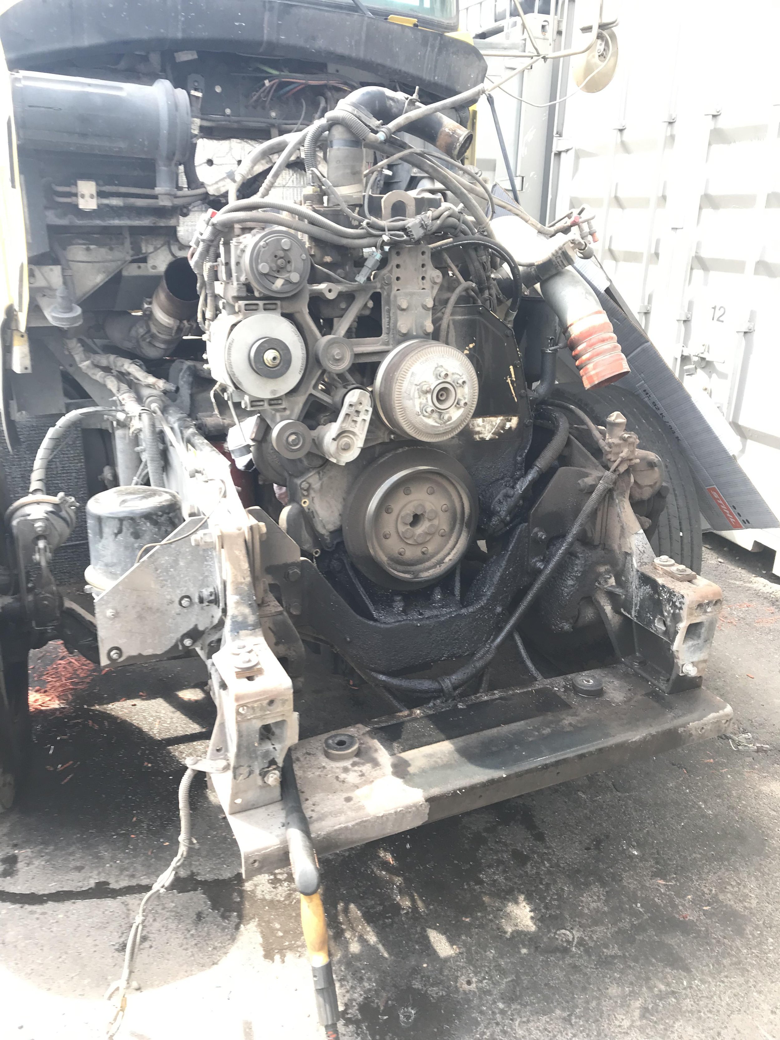 Image of a disassembled vehicle engine mounted on a metal frame inside a garage or repair shop.