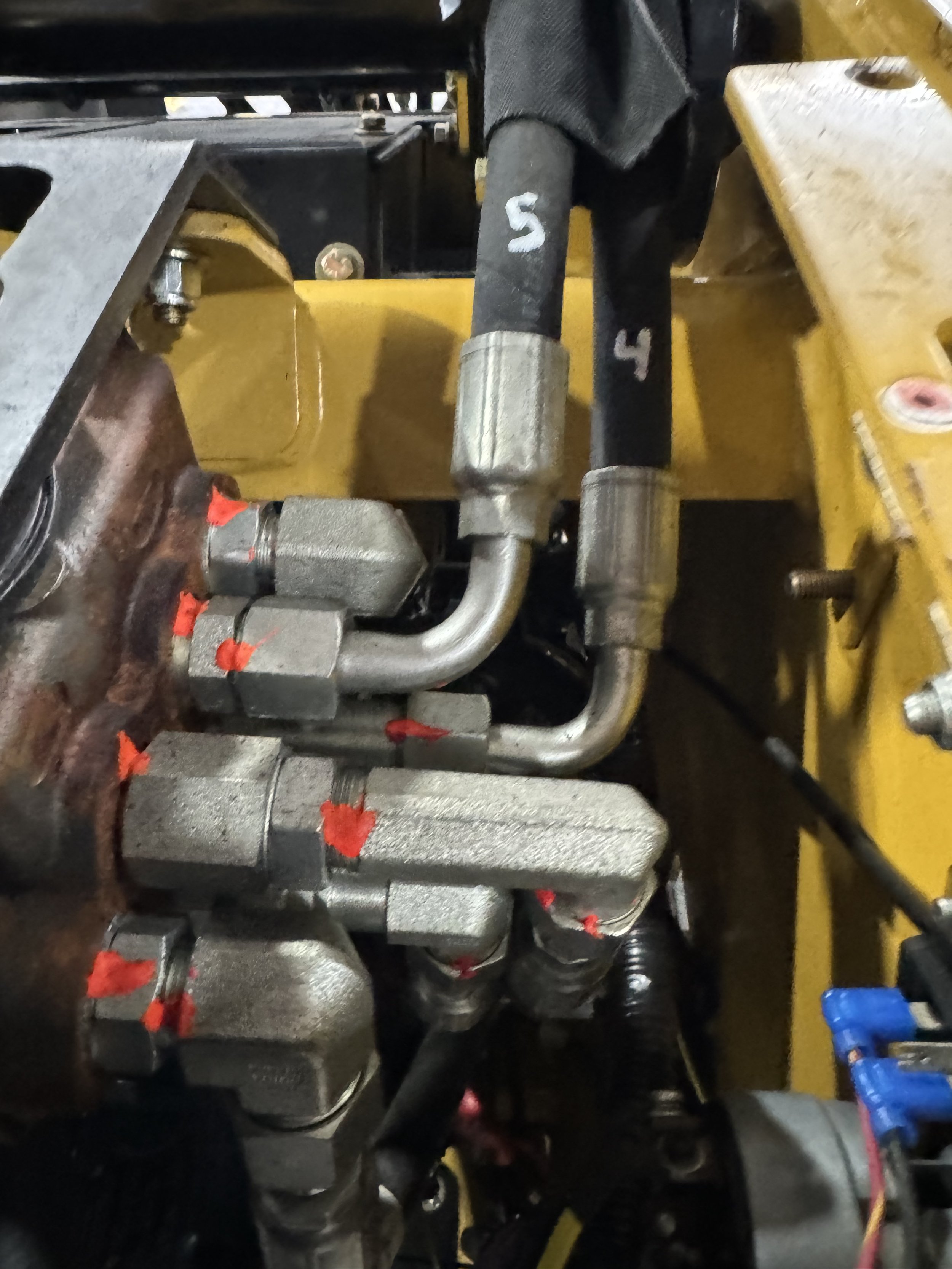 Close-up view of mechanical components, including metal pipes, valves, and a black fabric with white numbers 4 and 5 marked on it, part of machinery or equipment.
