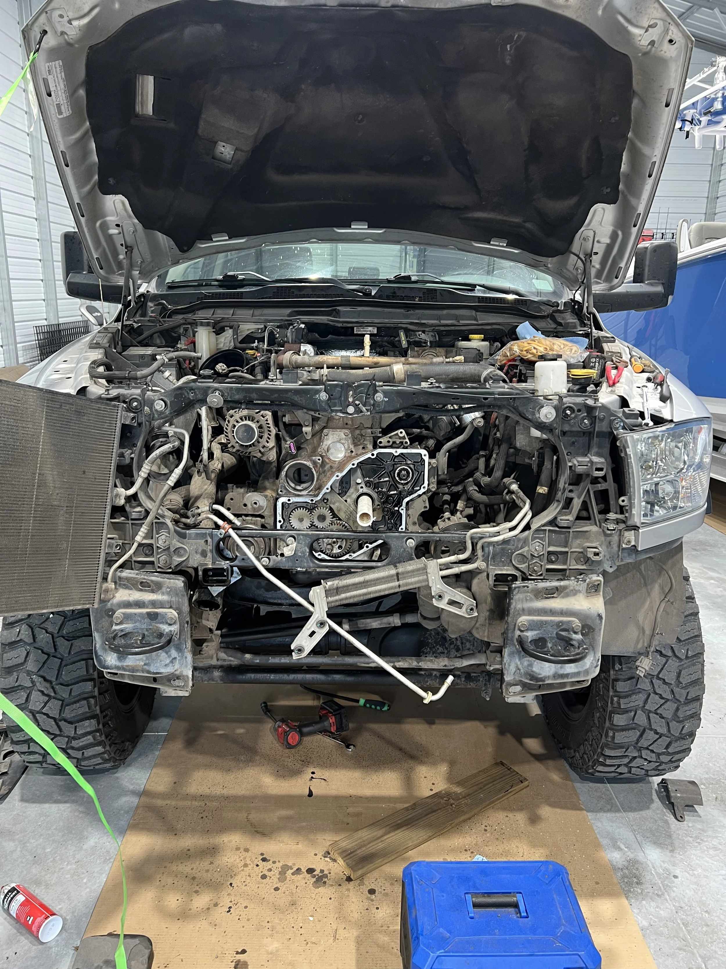 Front view of a vehicle with the hood open, showing the engine compartment and mechanical parts, on a workbench with tools and materials around.