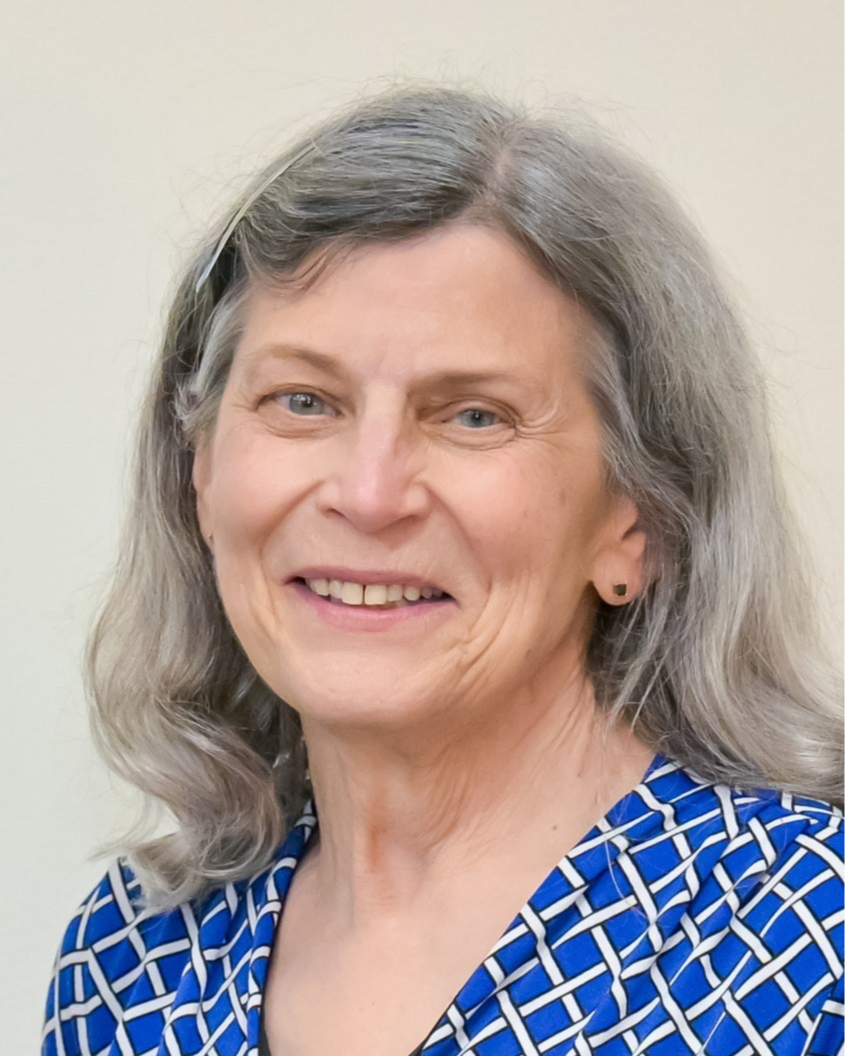 A smiling middle-aged woman with gray hair wearing a blue and white patterned top.
