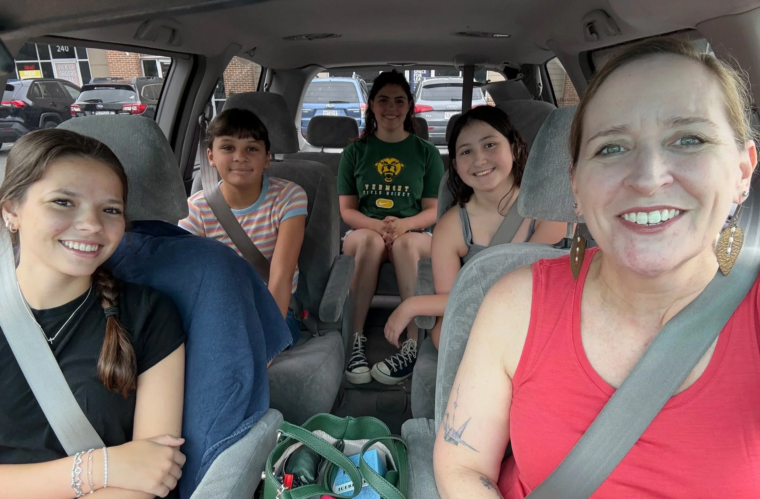 A woman and five children seated inside a vehicle, smiling at the camera.