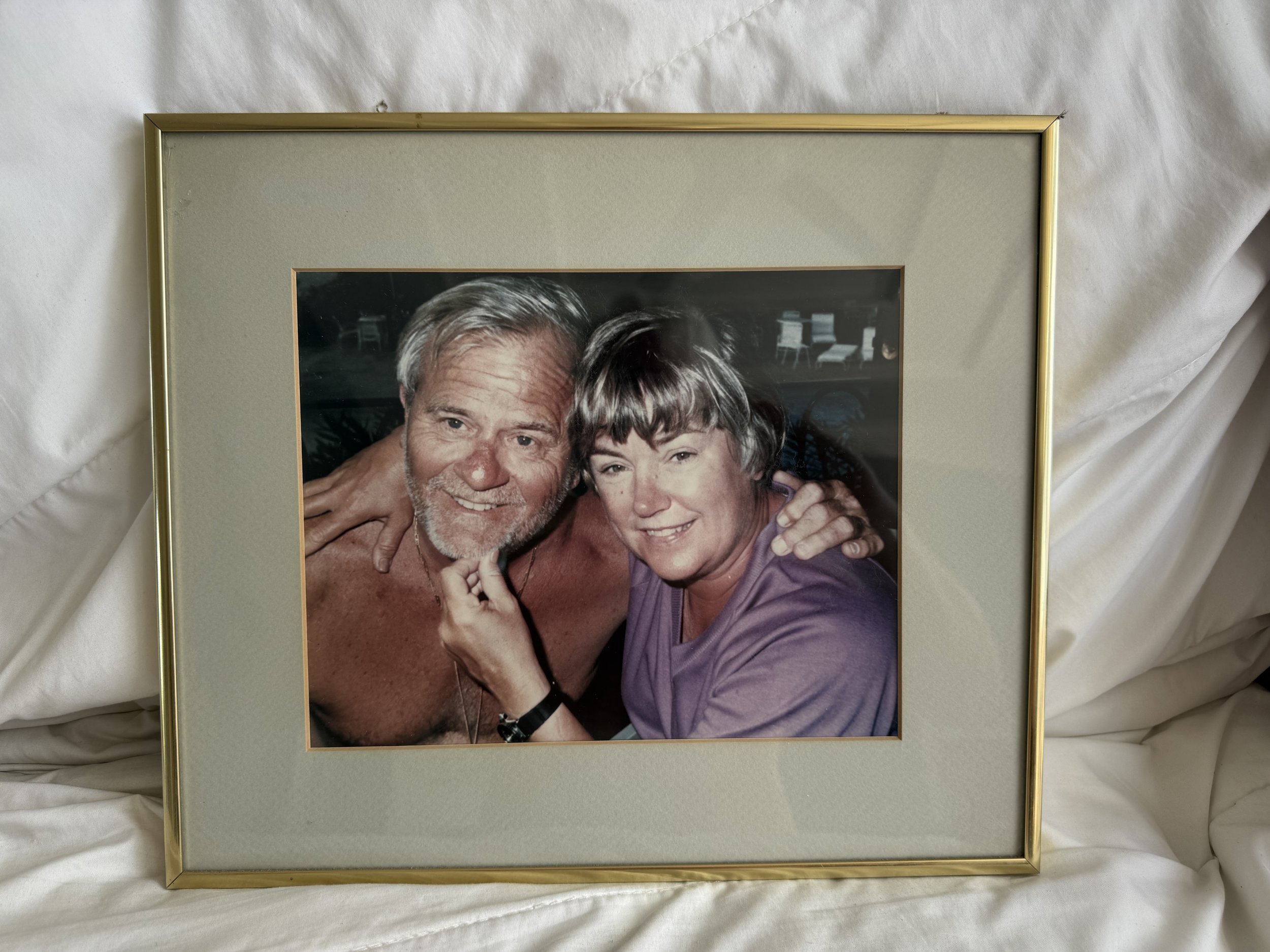 A framed photograph of an older man with gray hair and a beard, and an older woman with short gray hair, smiling and hugging each other.