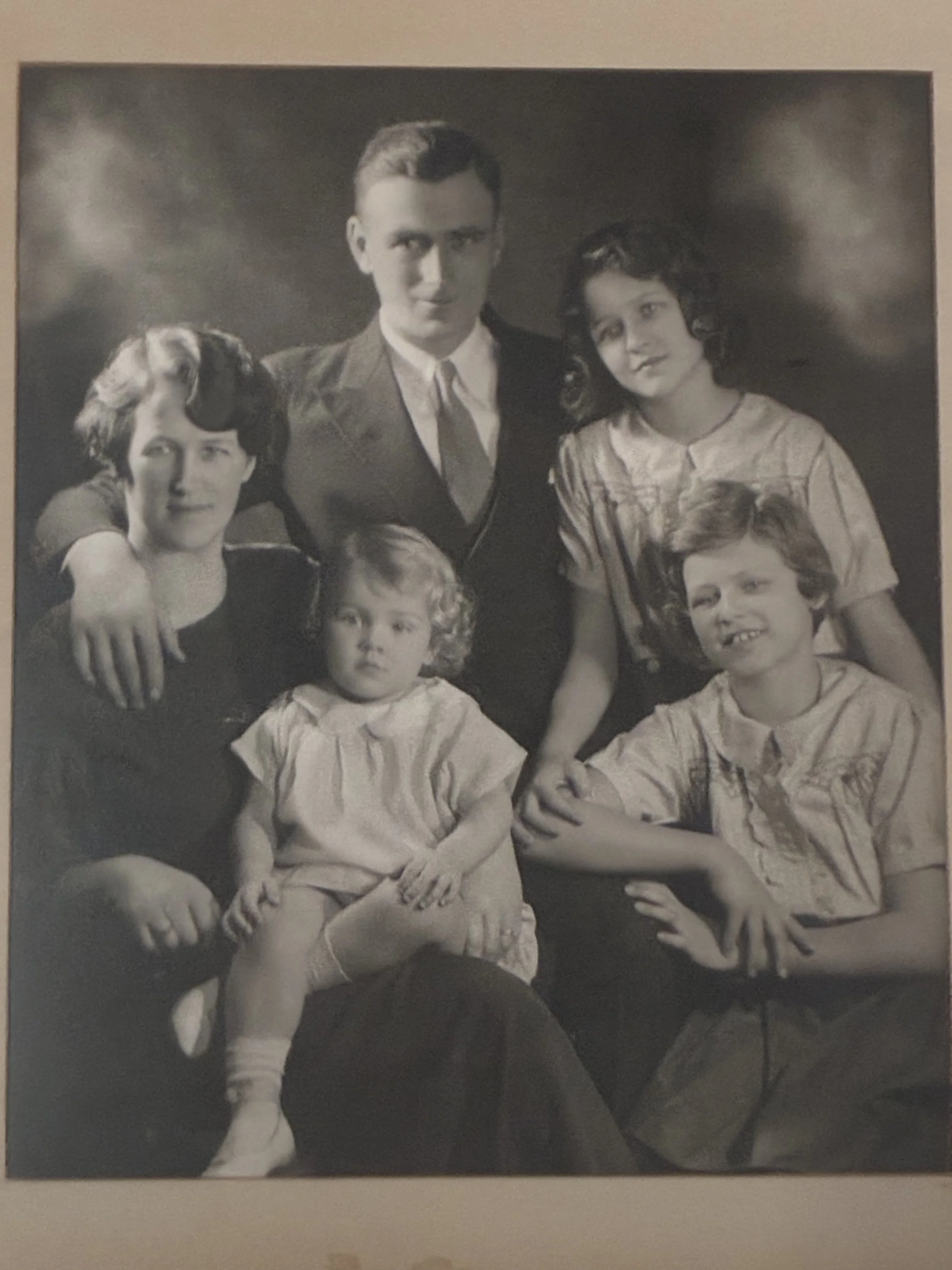 A black and white vintage family portrait featuring five people, including a woman, two children, and a man, posed together indoors.