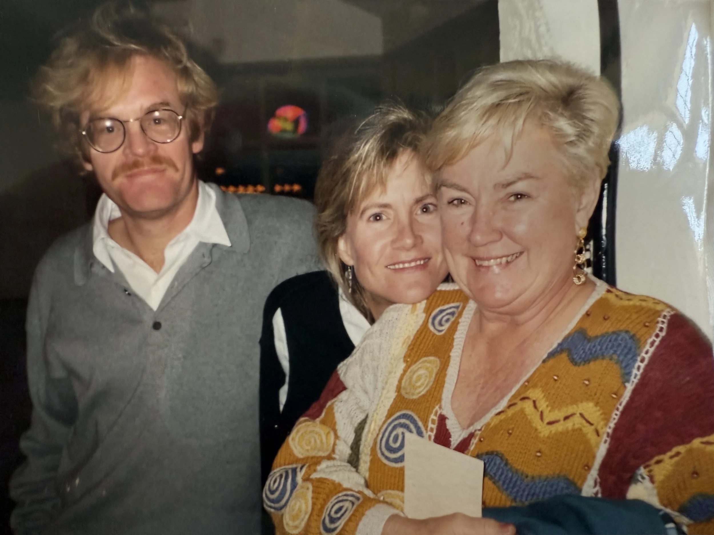 Three people smiling together, two women and one man, in a close-up indoor setting.