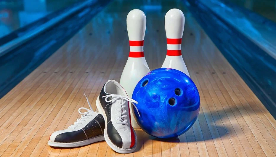 Bowling pins, a bowling ball, and a pair of bowling shoes on a bowling lane.