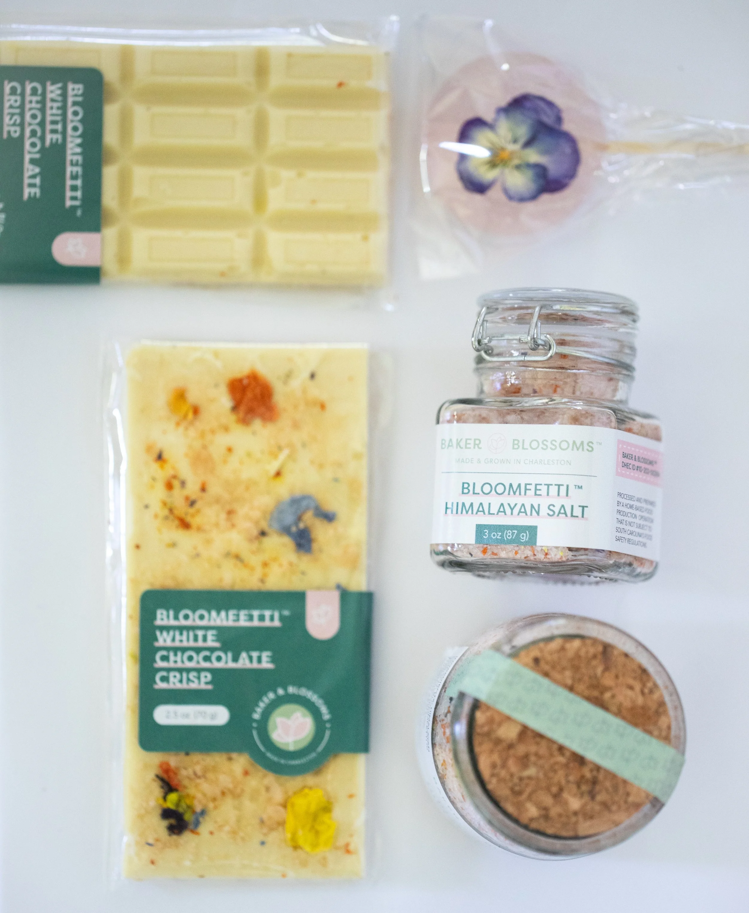 Assorted edible flower confections from Charleston pastry studio—white chocolate bar, botanical infused sugar, and bouquet lollipop available for wholesale and local gifting