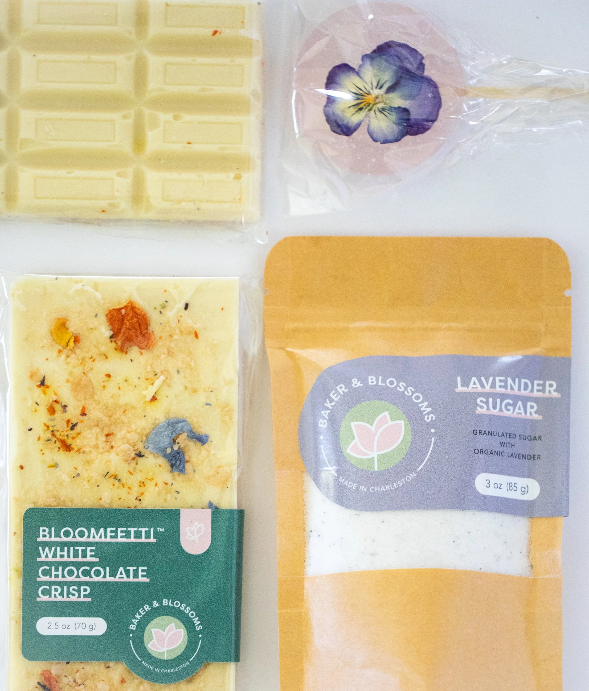Assorted edible flower confections from Charleston pastry studio—white chocolate bar, botanical infused sugar, and bouquet lollipop available for wholesale and local gifting