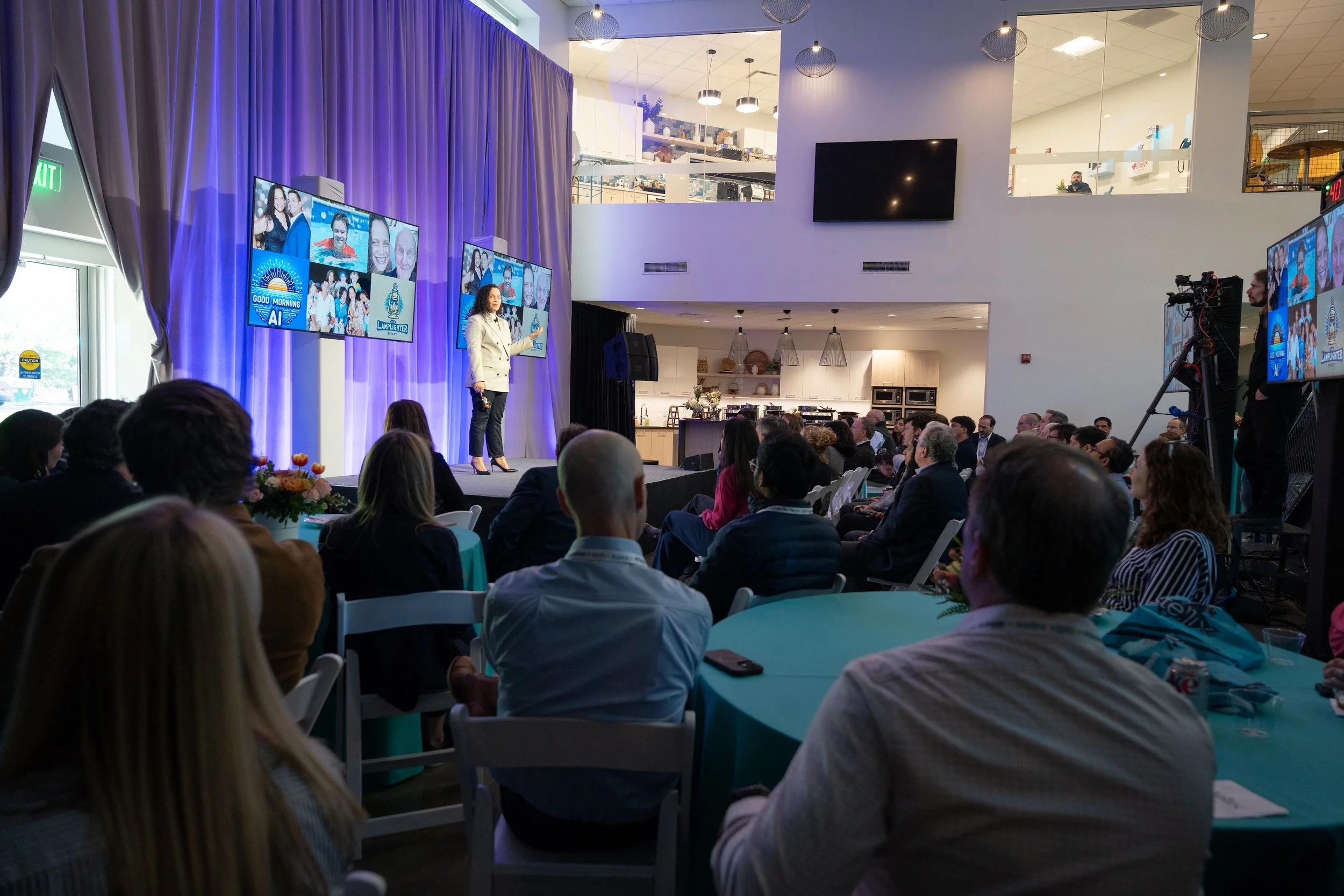 A woman is giving a presentation about AI on stage in front of an audience at Stellix's office, with screens displaying images and text. A camera operator films the keynote from the back.