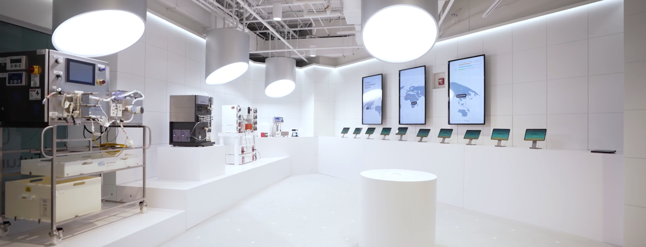 A frame from the Stellix Customer Engagement Center video - an all-white technology exhibit space displaying various industrial and scientific equipment, digital screens, and informational displays.